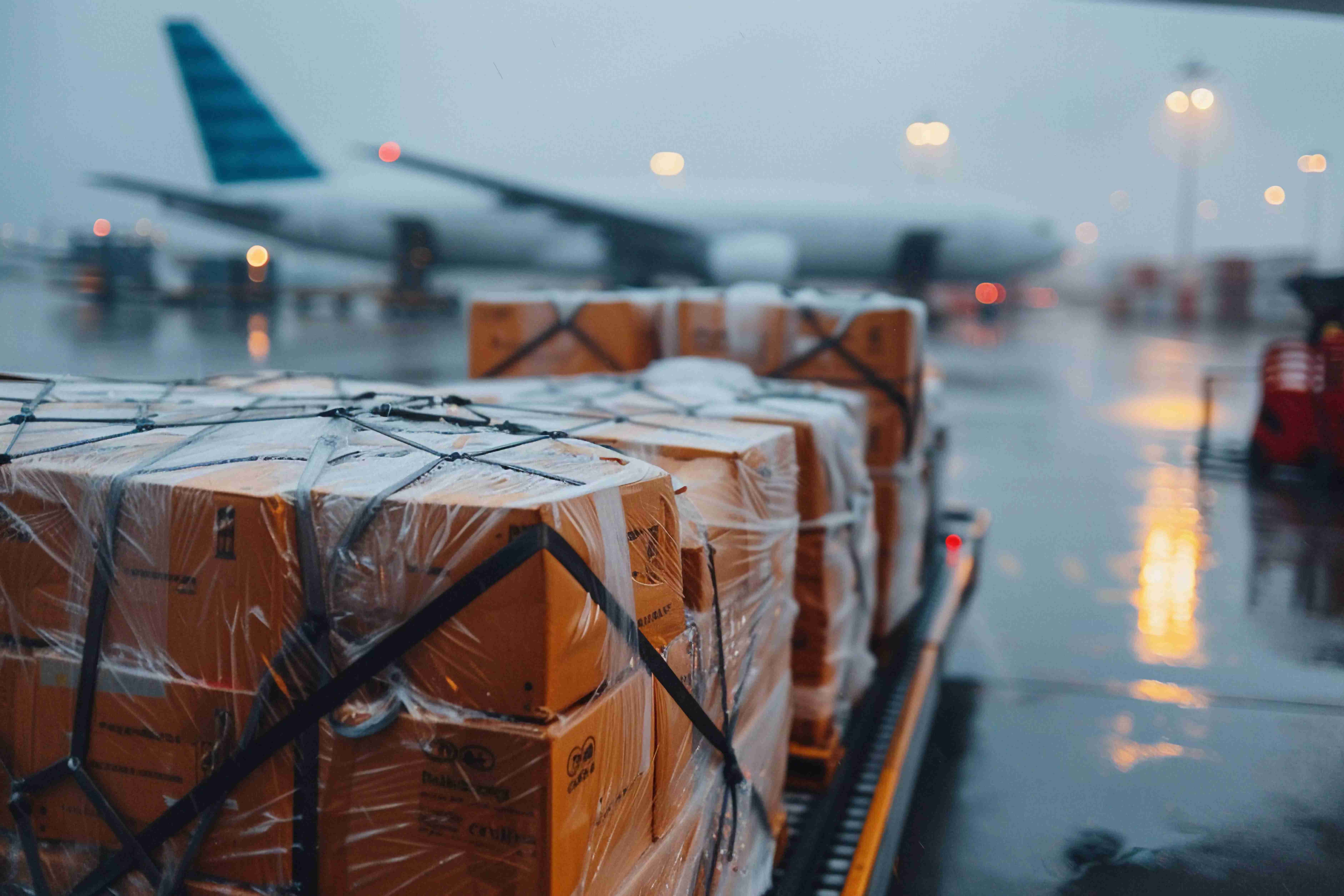 Air freight cargo pallets are prepared for international shipment on an airport runway during rain.