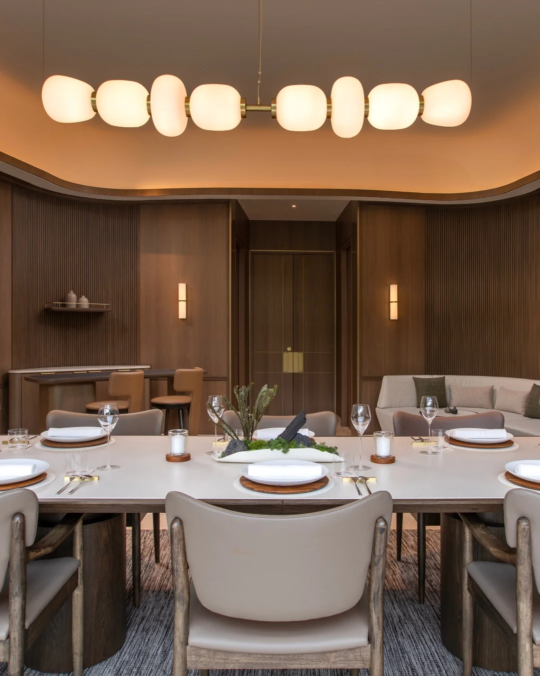 An elegant dining room setup at Potager featuring a large table with white plates and glasses, wooden chairs, and a soft-lit modern chandelier.