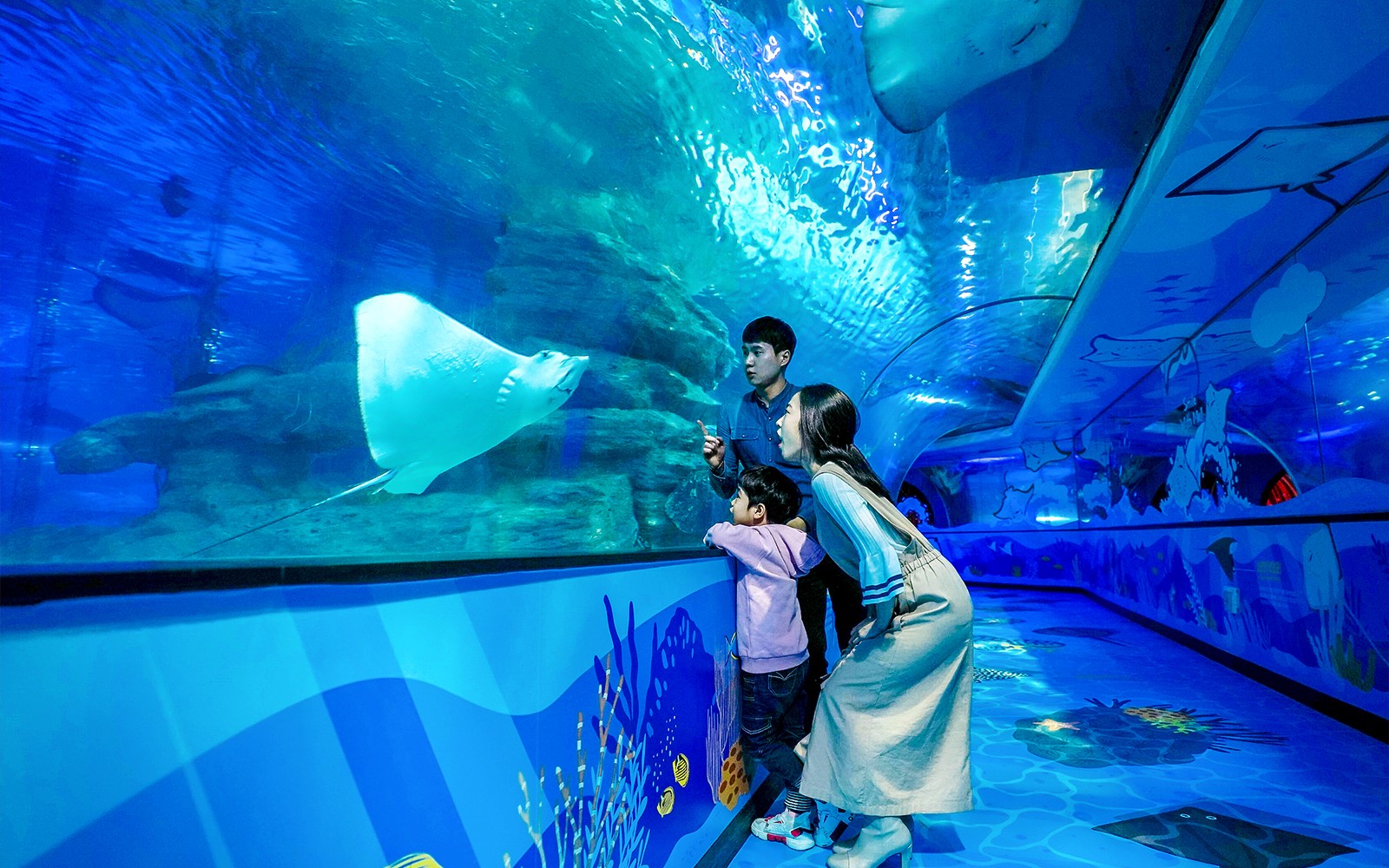 Family observing stingray at SEA LIFE Busan Aquarium tunnel.