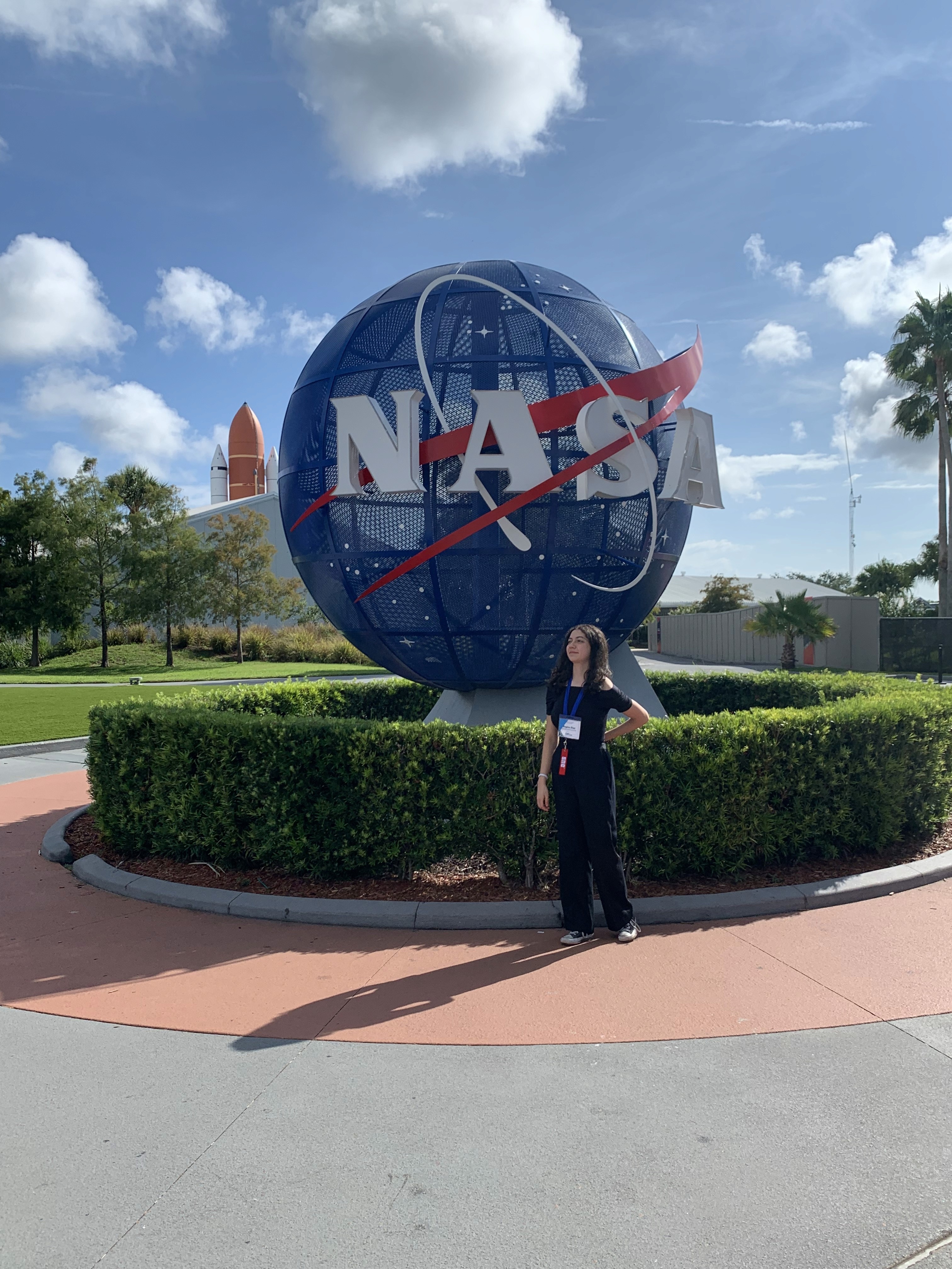 Regina stands in front of a NASA Meatball emblem outdoors.