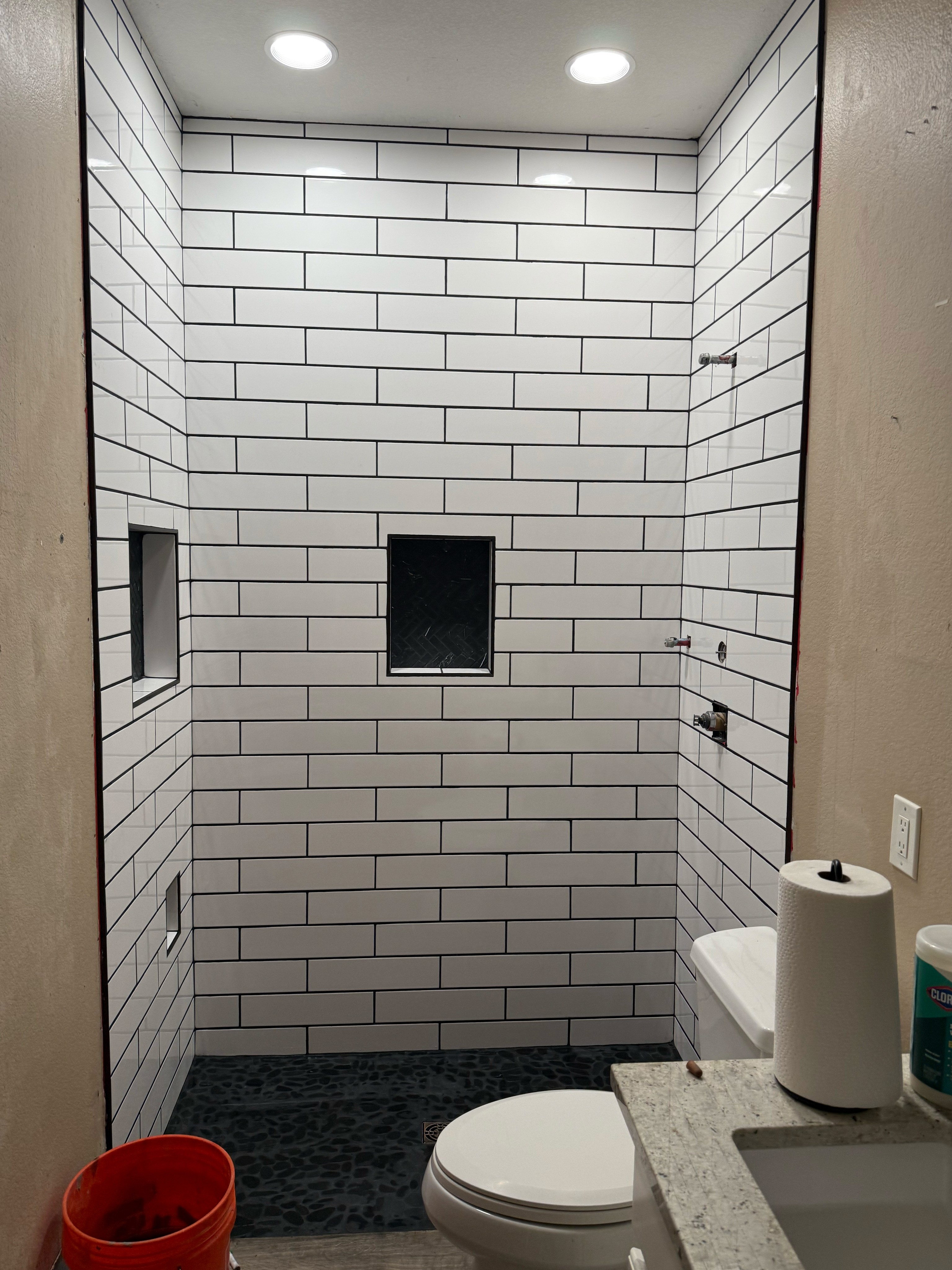 Modern shower with white subway tiles and contrasting black grout, two black built-in shower niches, and a dark mosaic tile shower floor.