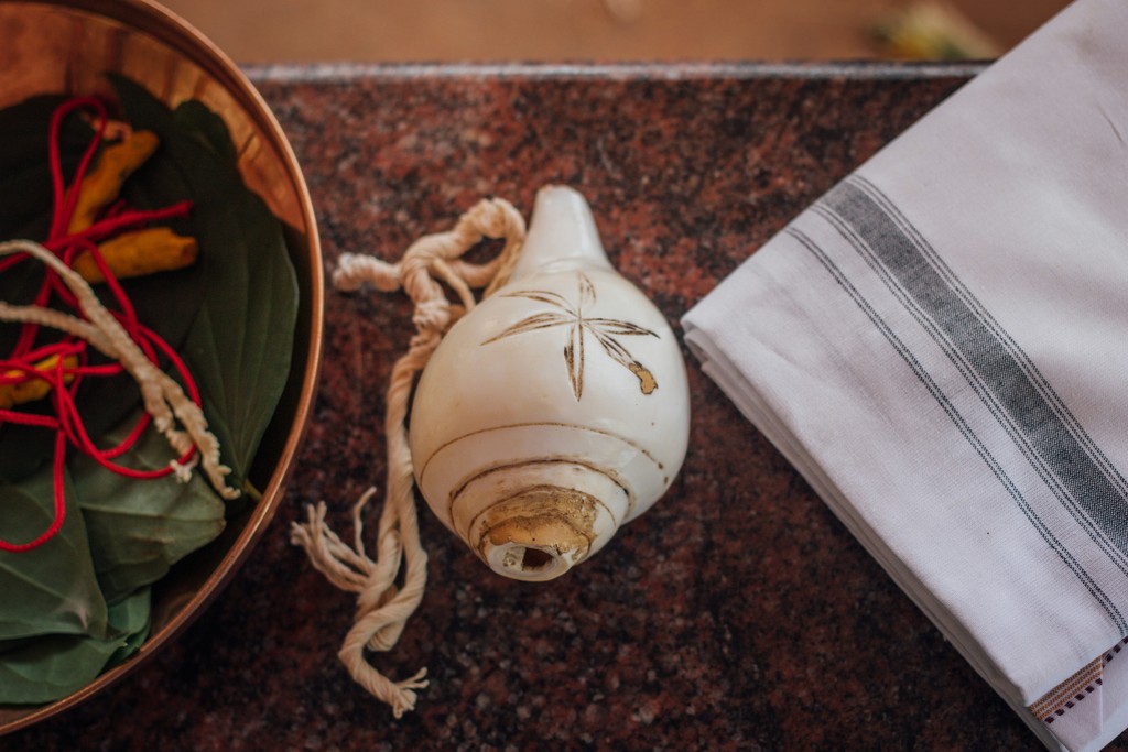 A traditional conch shell, a white cloth with grey stripes, and a bowl with leaves and red-tied objects on a brown marble surface, symbolizing cultural rituals and heritage.