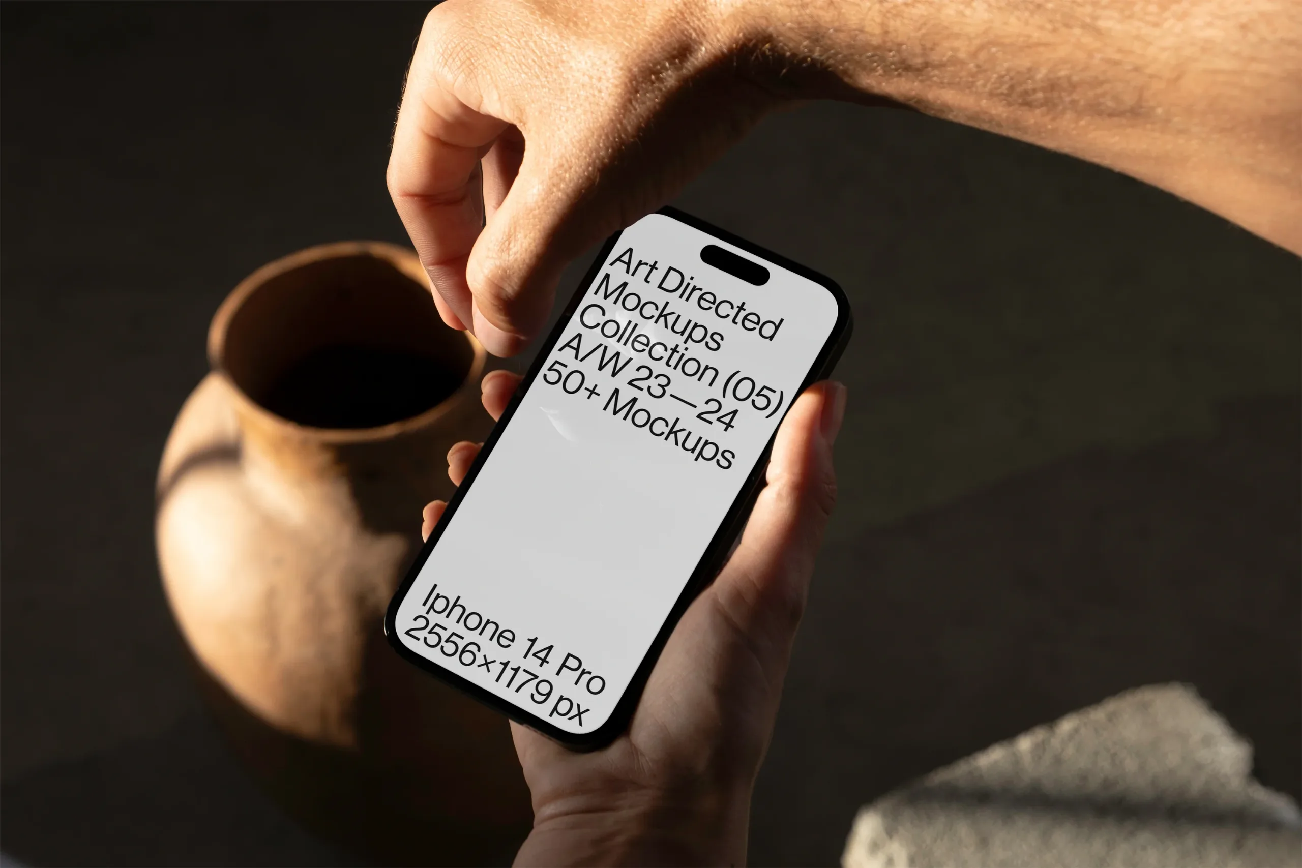 iPhone 14 Pro mockup in hand, featuring an amber screen in a natural setting. A clay pot and stone surfaces are in the background, illuminated by soft, warm natural light.
