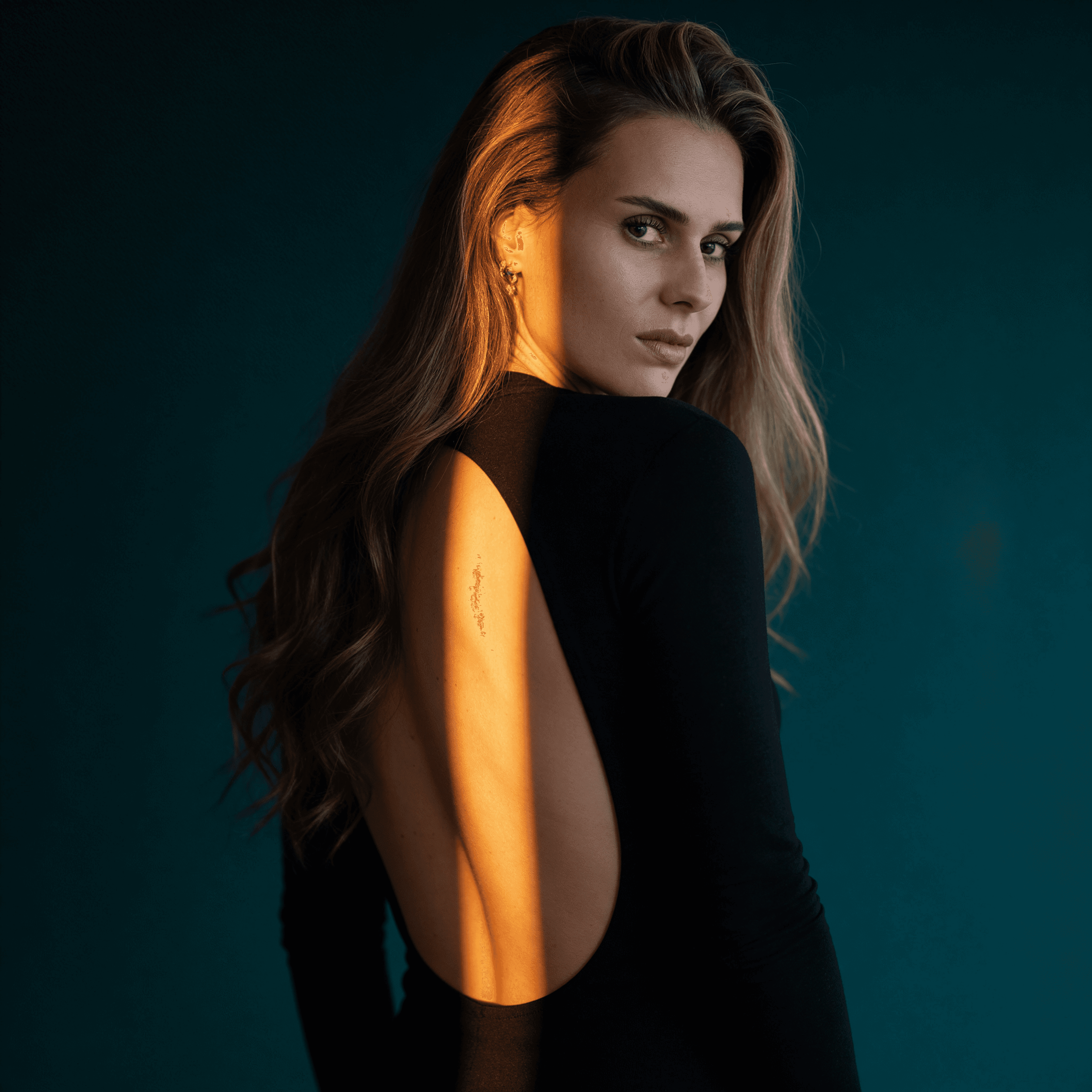 Weibliches KI-Model – Digitaler Zwilling von Trickhouse, schwarzes rückenfreies Kleid, goldene Ohrringe, dramatischer Lichtstreifen, Blick über die Schulter, dunkler Studiohintergrund, KI-Model-Agentur Düsseldorf.