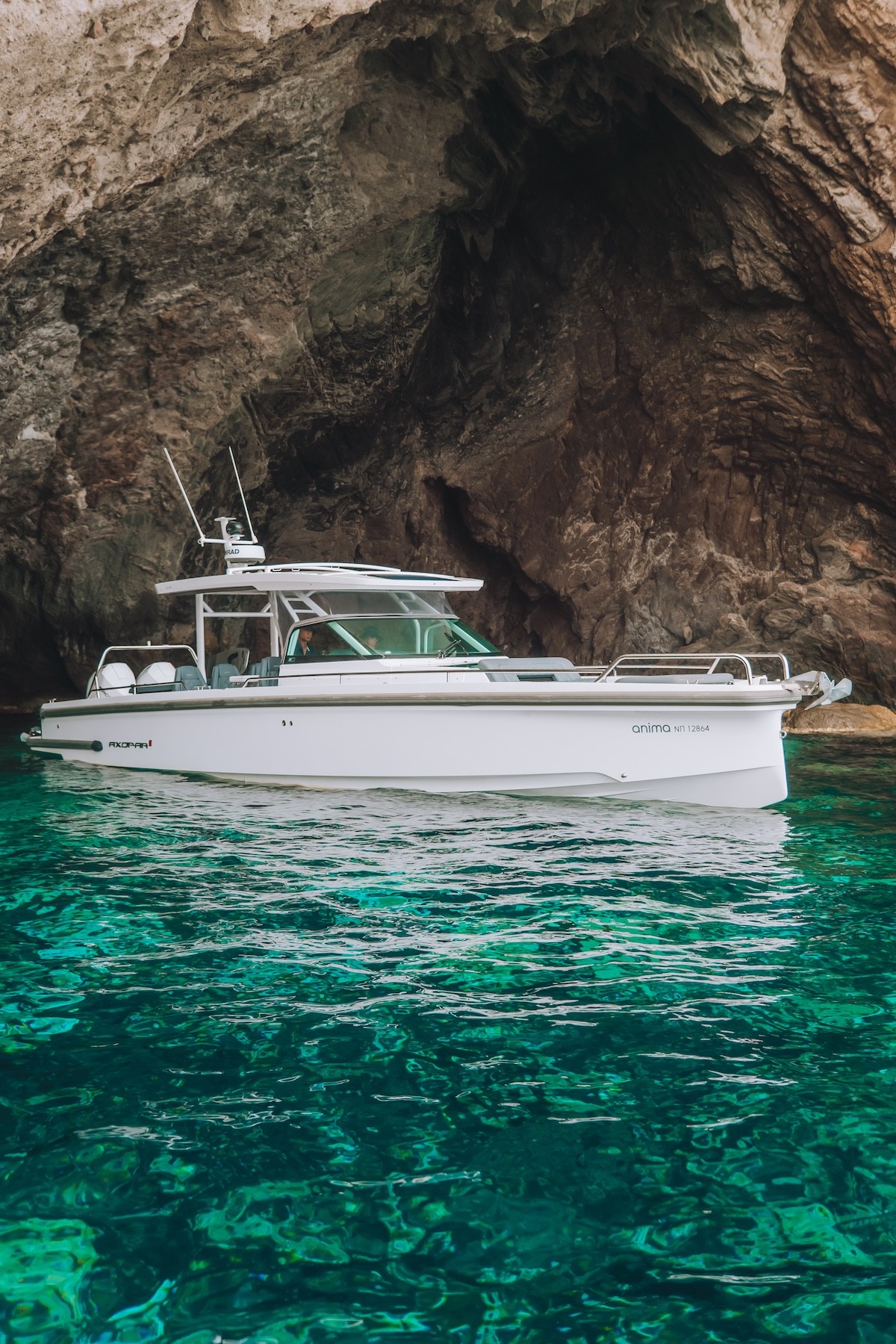 White Axopar 37 yacht anchored in turquoise waters near dramatic limestone cliffs in the Cyclades.