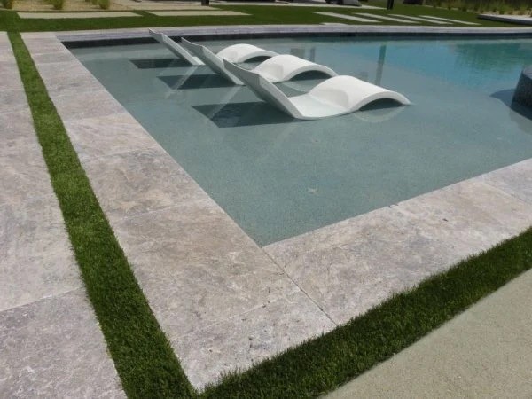 Sunlit edge of a pool with water and tile detail