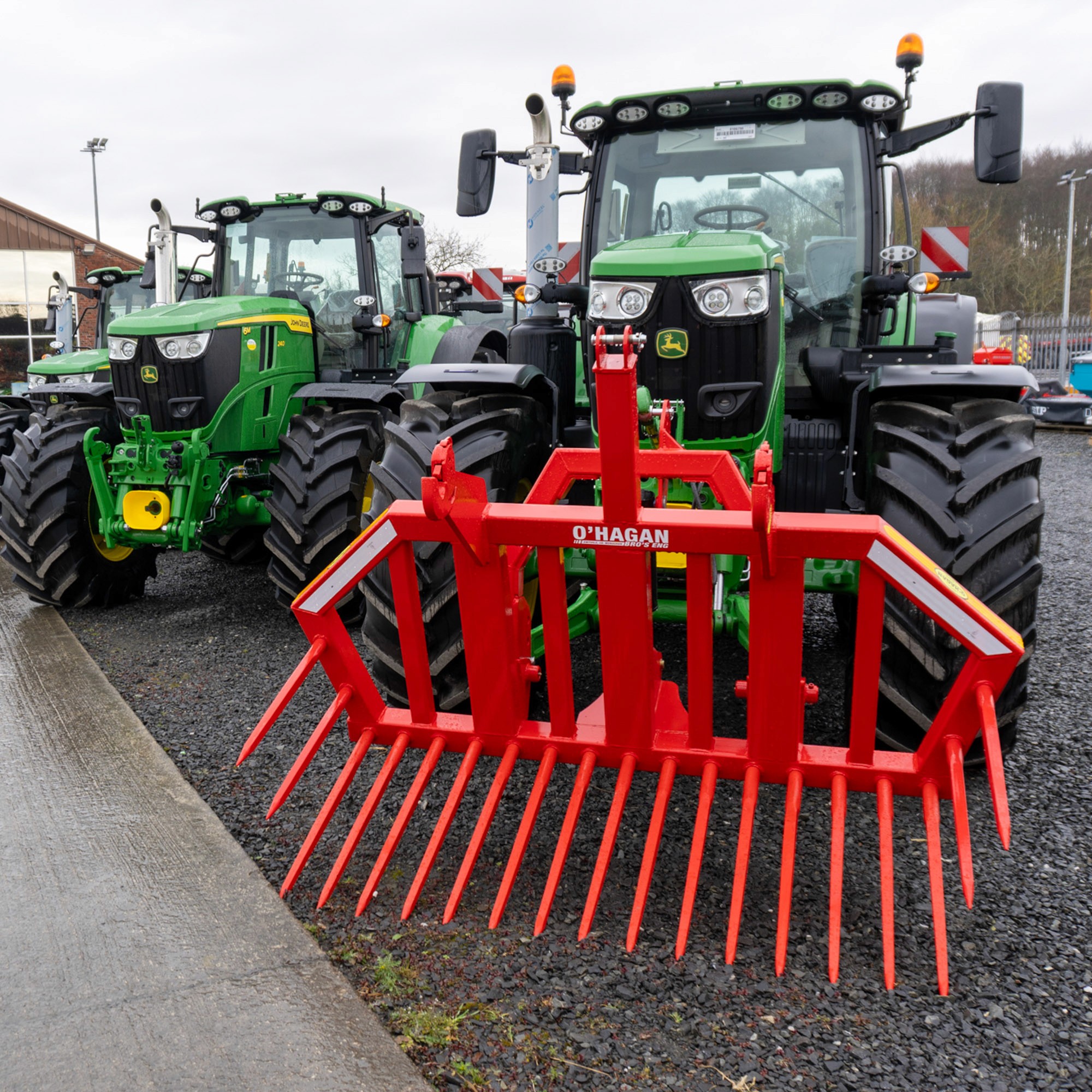 Red Stone fork attached to a Green John Deere parked beside another green John Deere on gravel