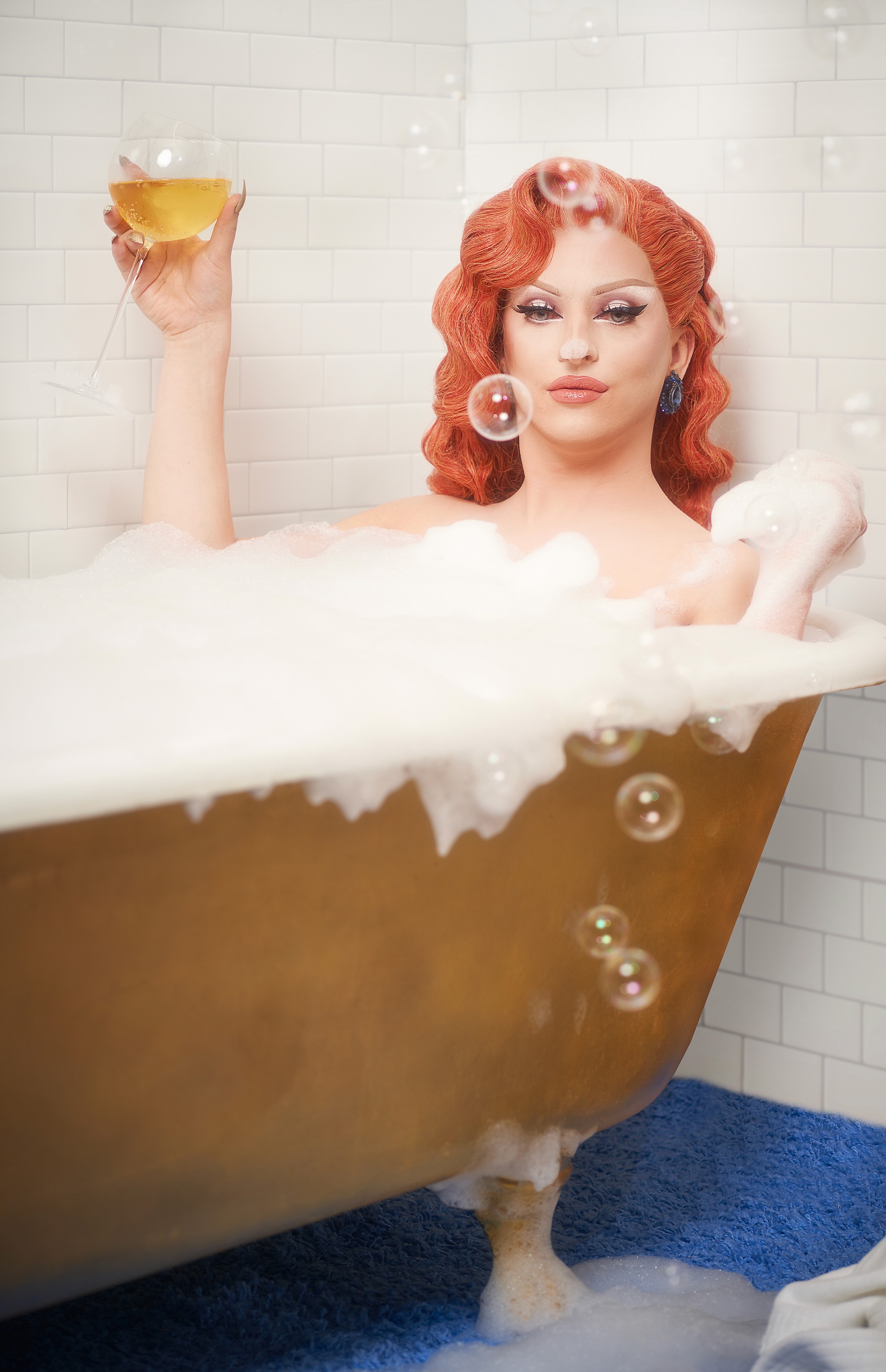 Miz Cracker raising a wine glass above an ornate gold bathtub
