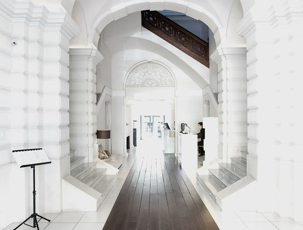 Heller Gang in einem Gebäude mit Holzboden und Treppe. Eine Person steht im rechten Fenster.