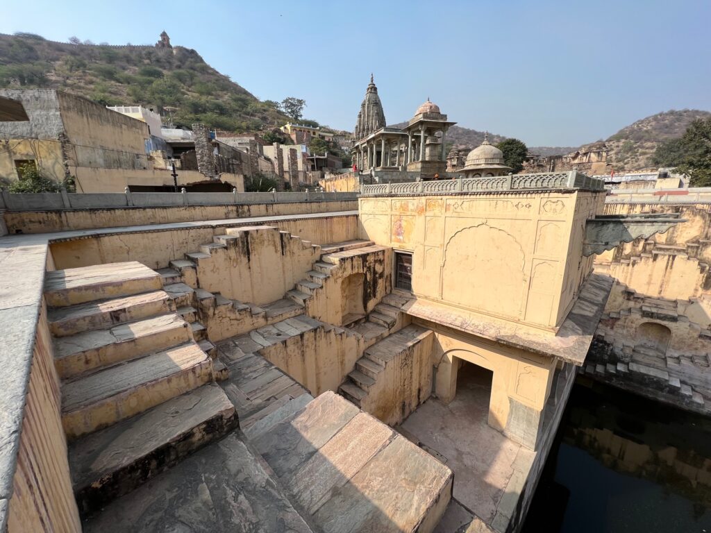 The steps of the step well from one side along a building near the water body and a temple in the distance.