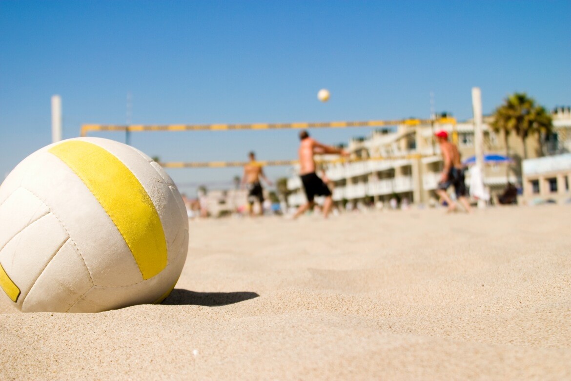 a close up of a beach volleyball with 4 players playing on a sand beach volleyball court
