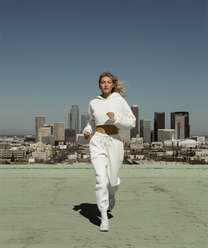 A woman in a white sweatsuit runs on a rooftop with a city skyline behind her