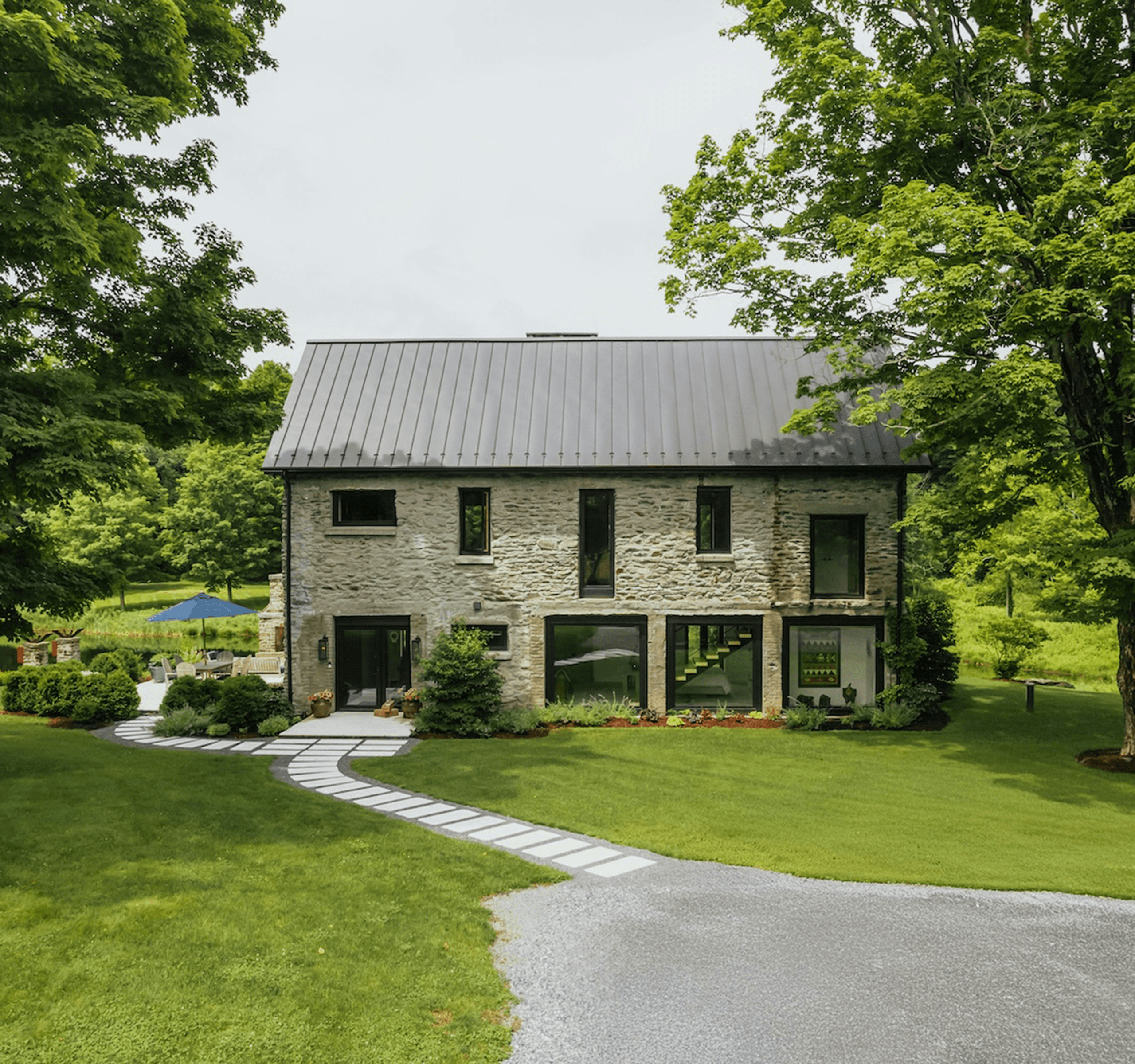 A modern house with a stone exterior, surrounded by lush green trees and a well-maintained lawn.