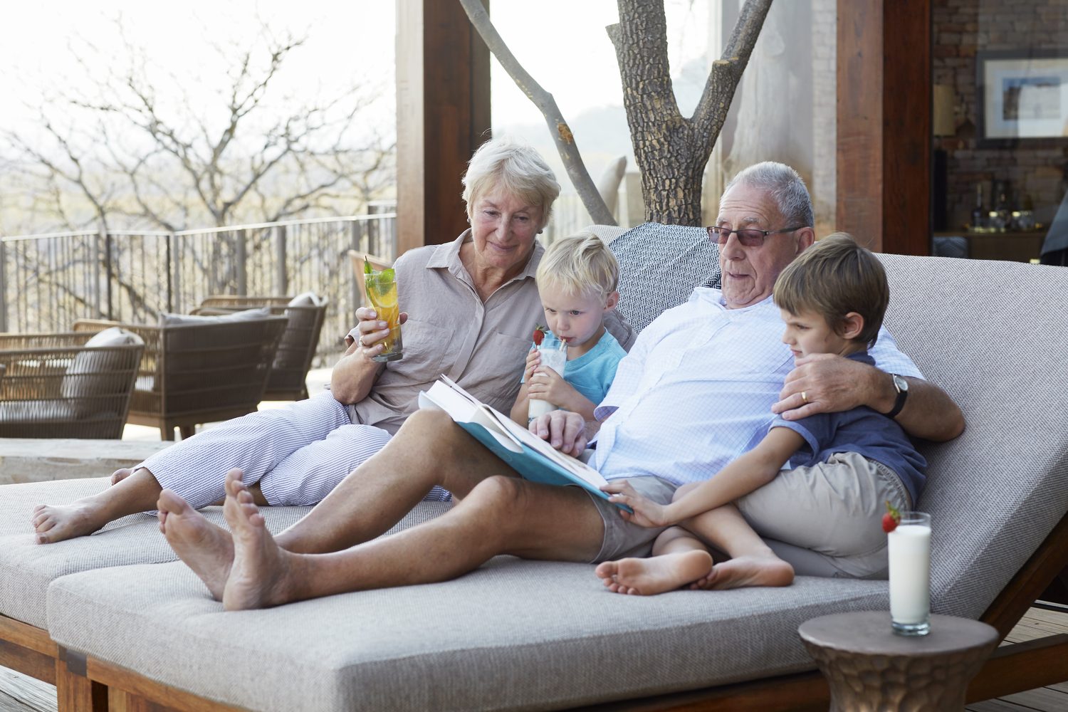Grandparents reading a picture book with their two grandsons on a shaded daybed