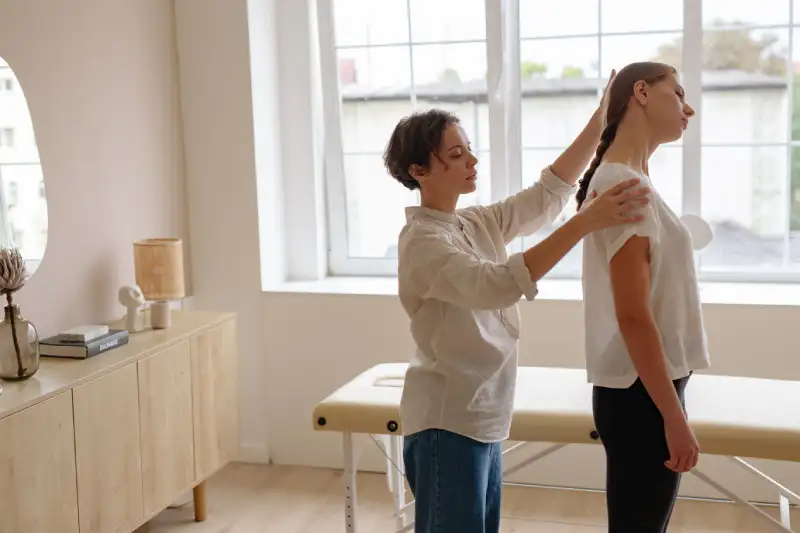 Physical therapist assessing a patient's posture and upper back alignment in a clinic"