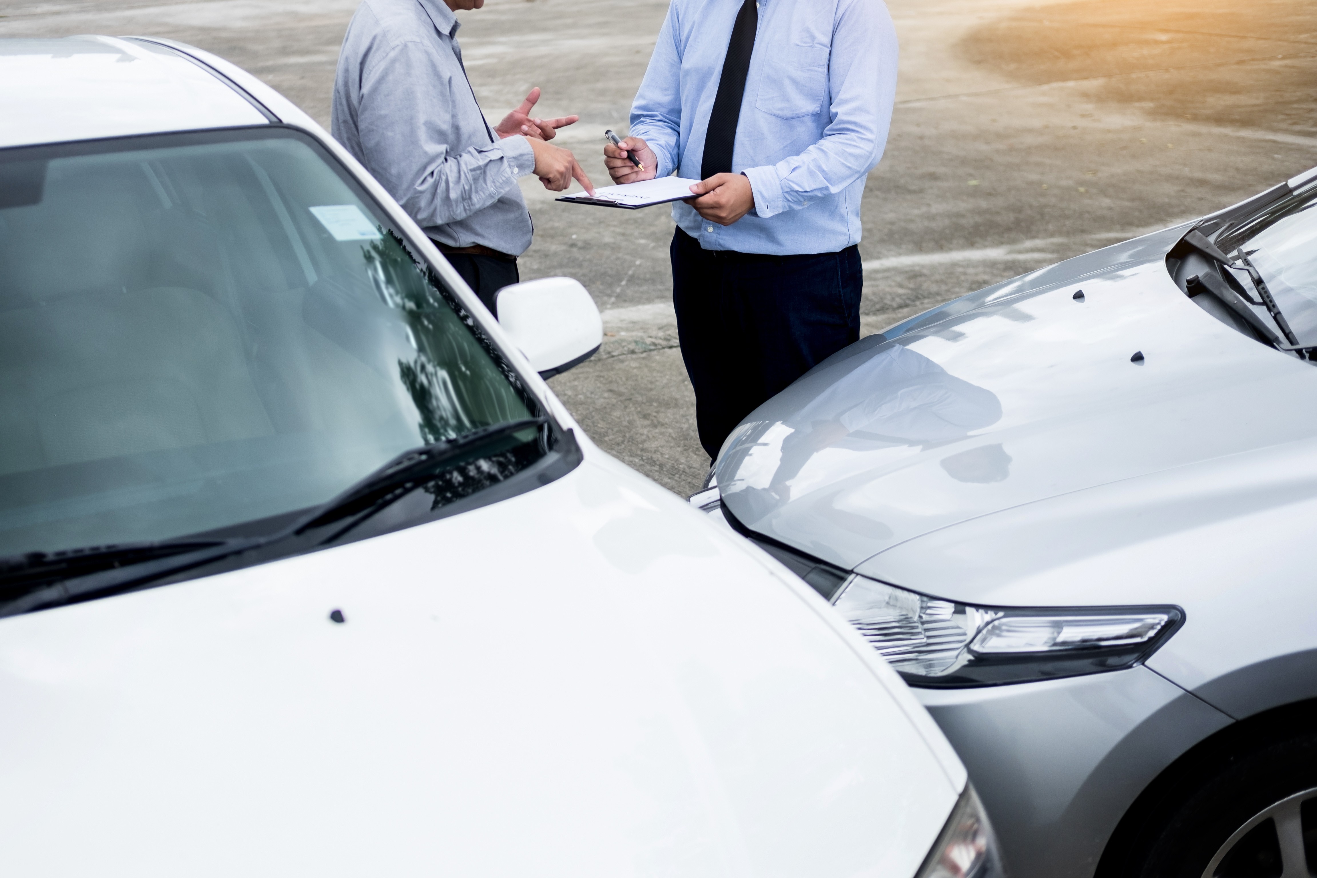 two men talking and looking at clipboard at scene of car accident