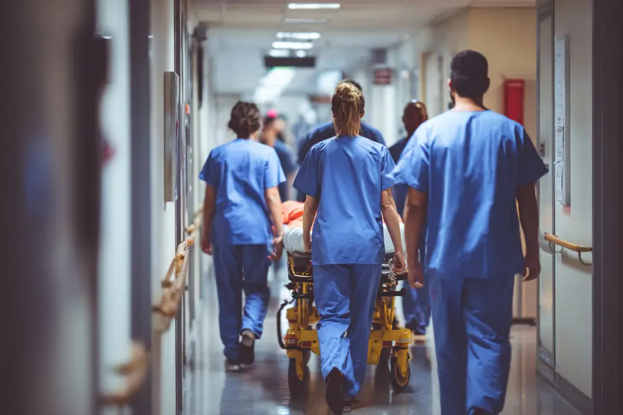 Clinical decision support AI aids hospital staff transporting patient on stretcher through busy medical hallway.