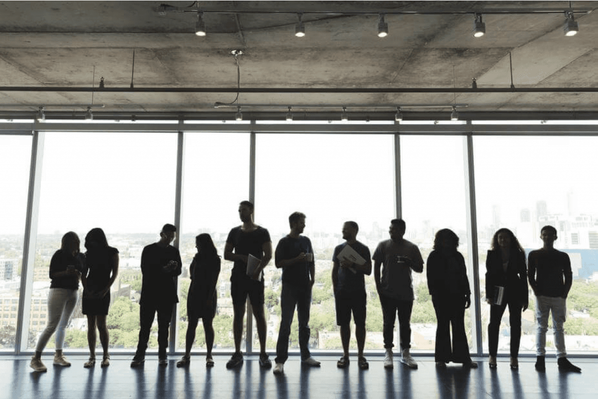 A group of people stood in a row, silhouetted against a large window in an industrial space