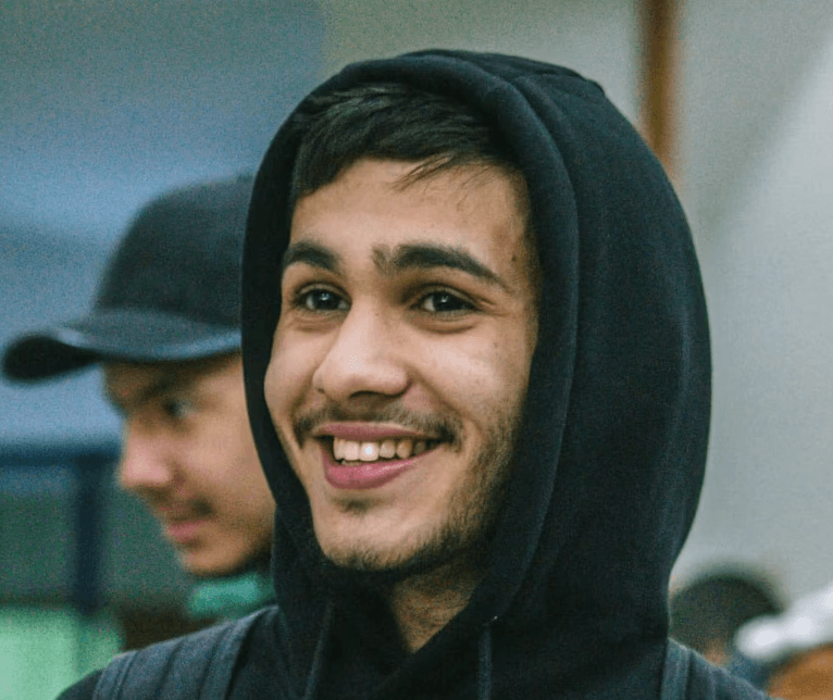 a young man wearing glasses standing in front of a mountain