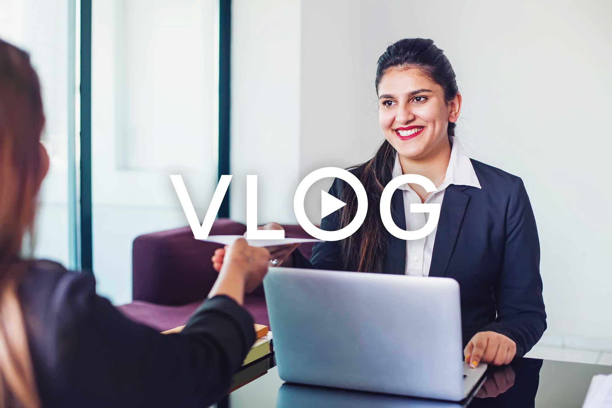 A person walks in front of large stone arches with dark doors, flanked by tall columns, in a historic building.