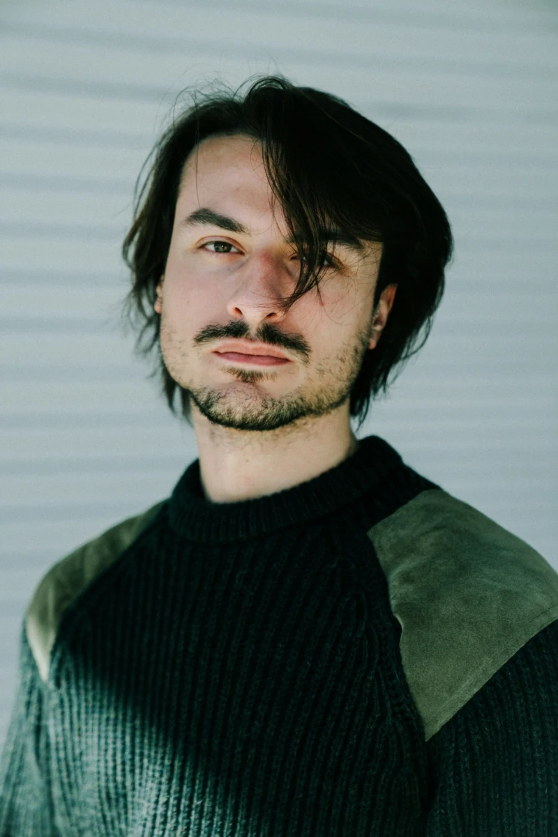a man in a black hoodie standing in front of a tree