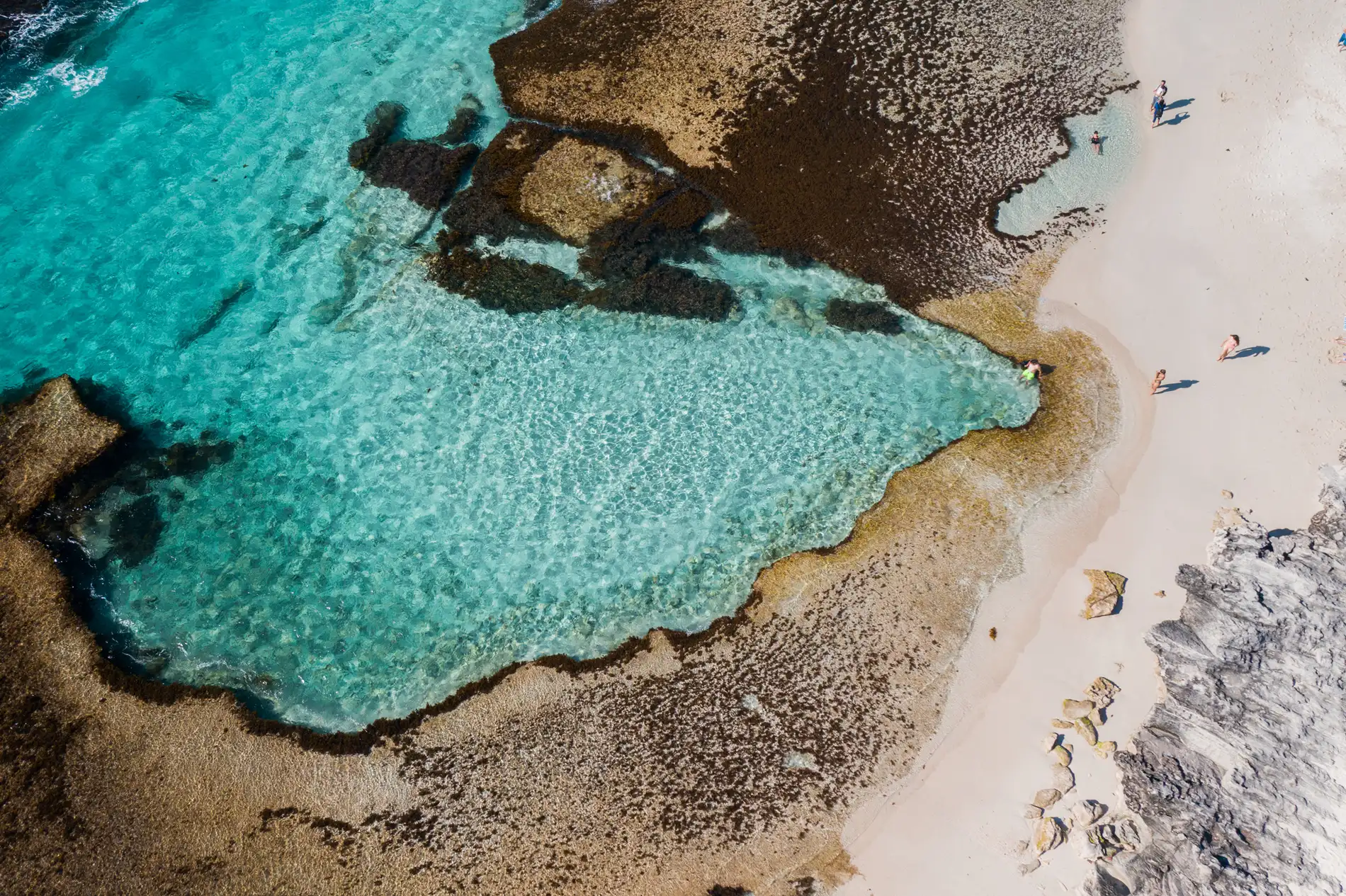 Aerial of a sheltered reef pool in bright turquoise water beside a white beach