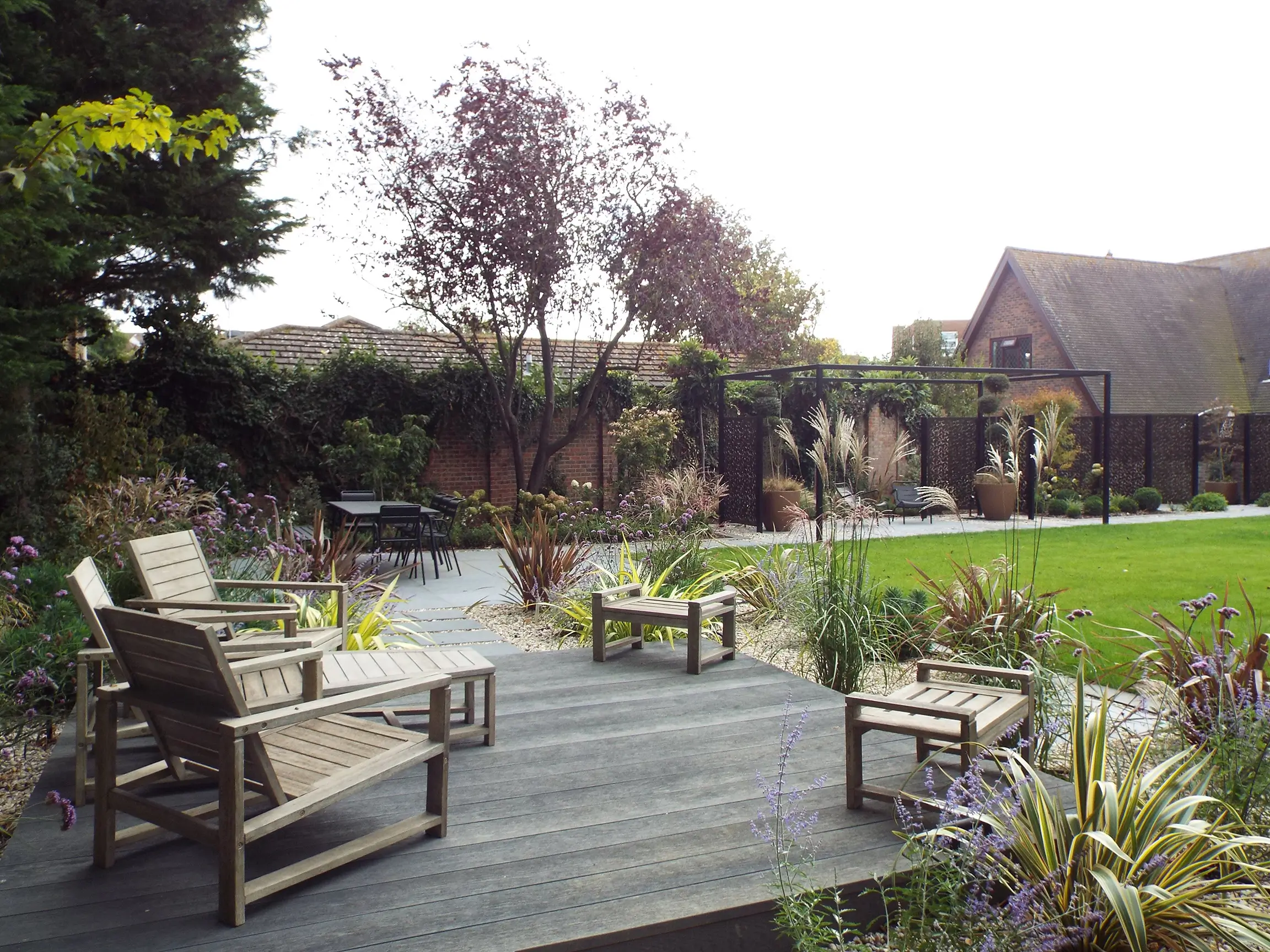A peaceful garden scene featuring wooden furniture, lush greenery, and a rustic shed in the background.