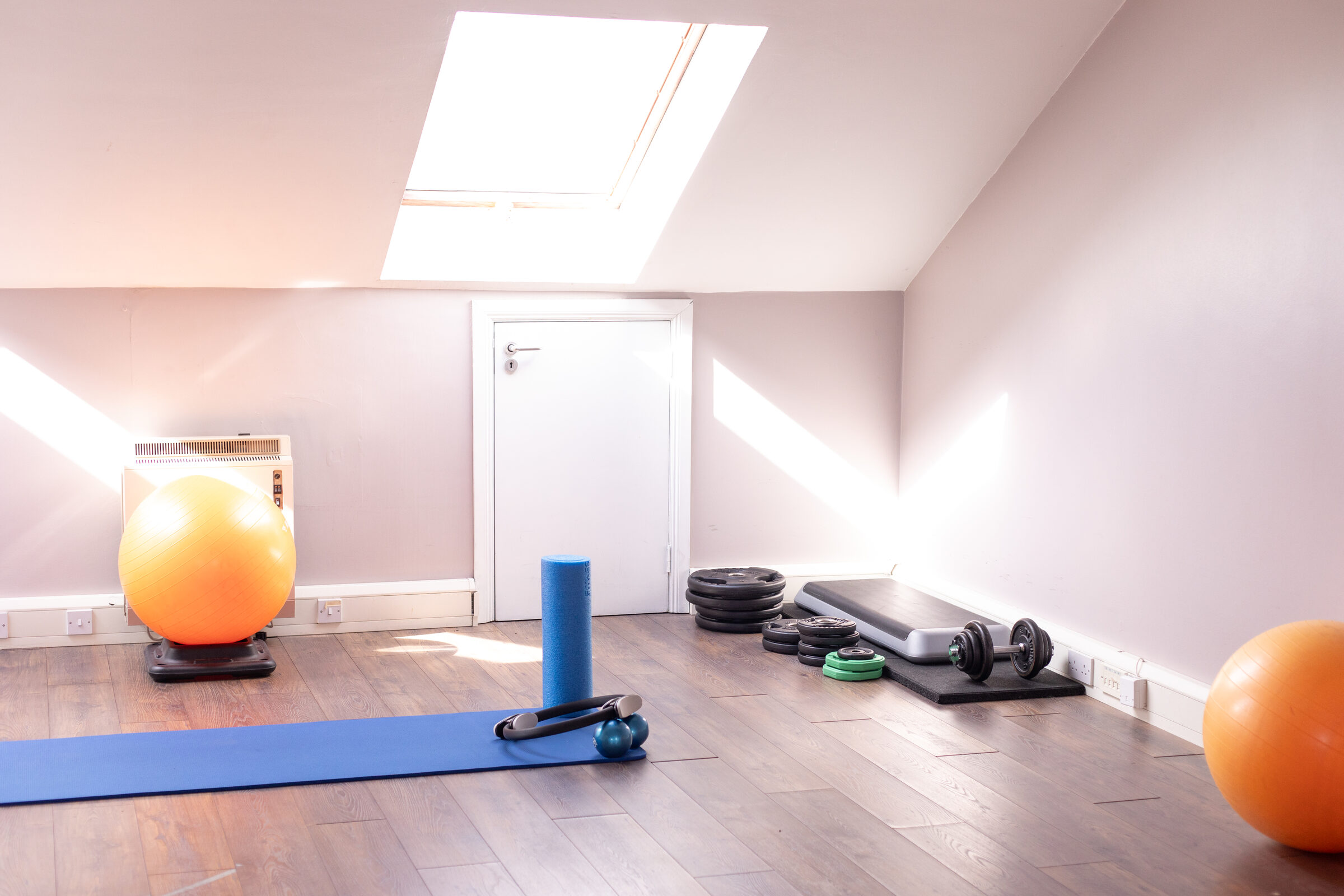 The gym at Total Physio, with an orange gym ball, a blue foam roller, an exercise mat and weights, lit by a skylight.