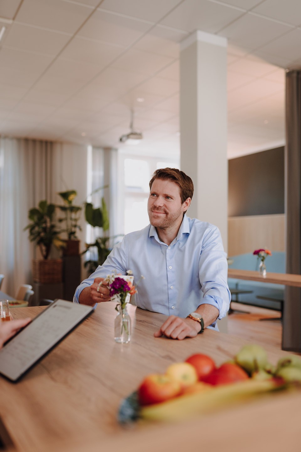 Männlicher Geschäftsführer im hellen Hemd sitzt im Gespräch an einem Tisch in einem freundlich eingerichteten Büro von SLB.