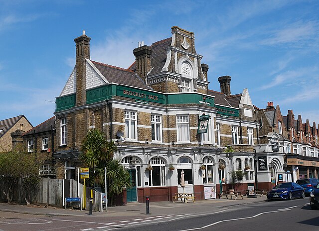 A smiling man with curly hair is sitting at a desk, looking at the camera, with a laptop and a lamp in the background.