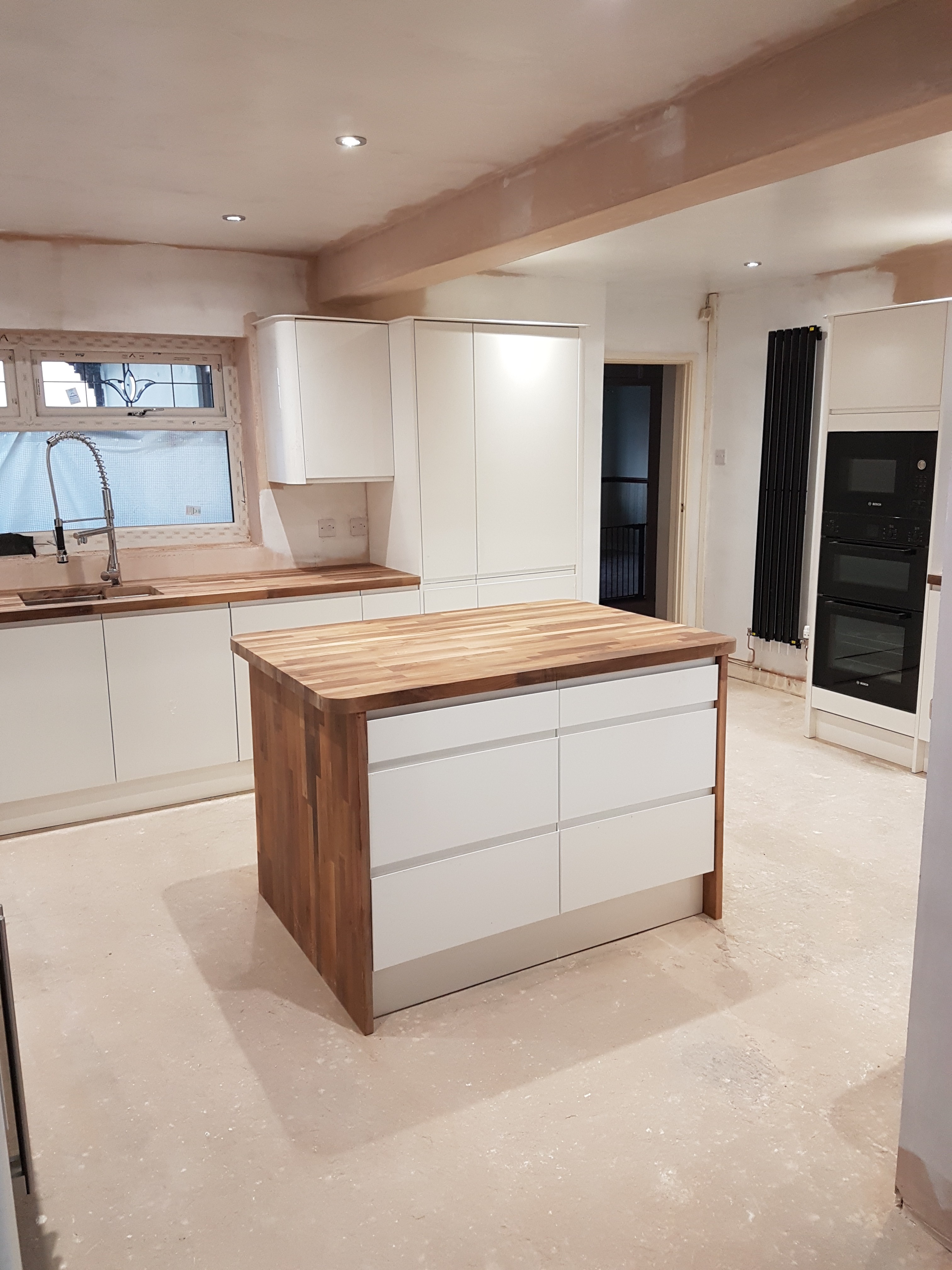 Modern living room with abstract art, beige sectional sofa, indoor plants, and large windows.