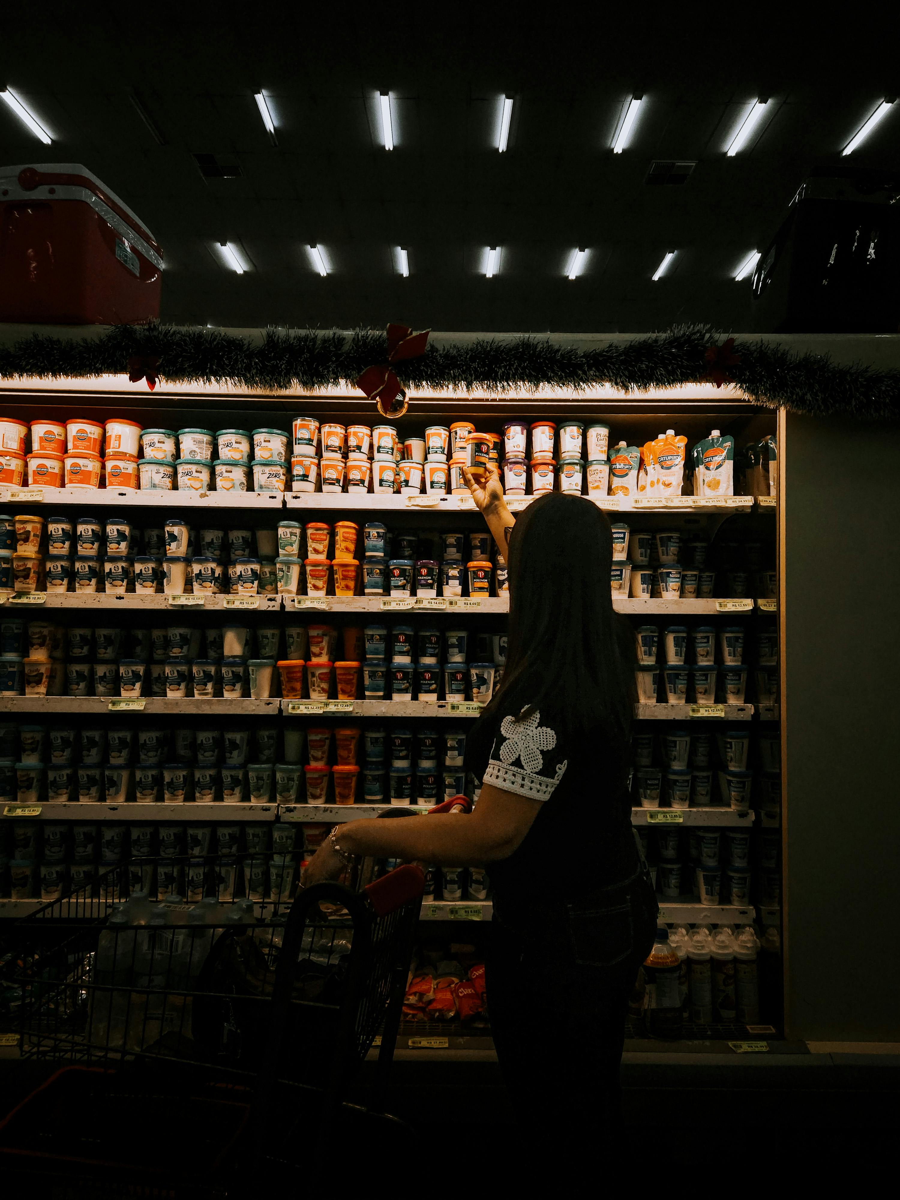 a-woman-shopping-at-a-grocery-store,-reaching-for-an-item-on-a-shelf. - pâm-santos (pexels)