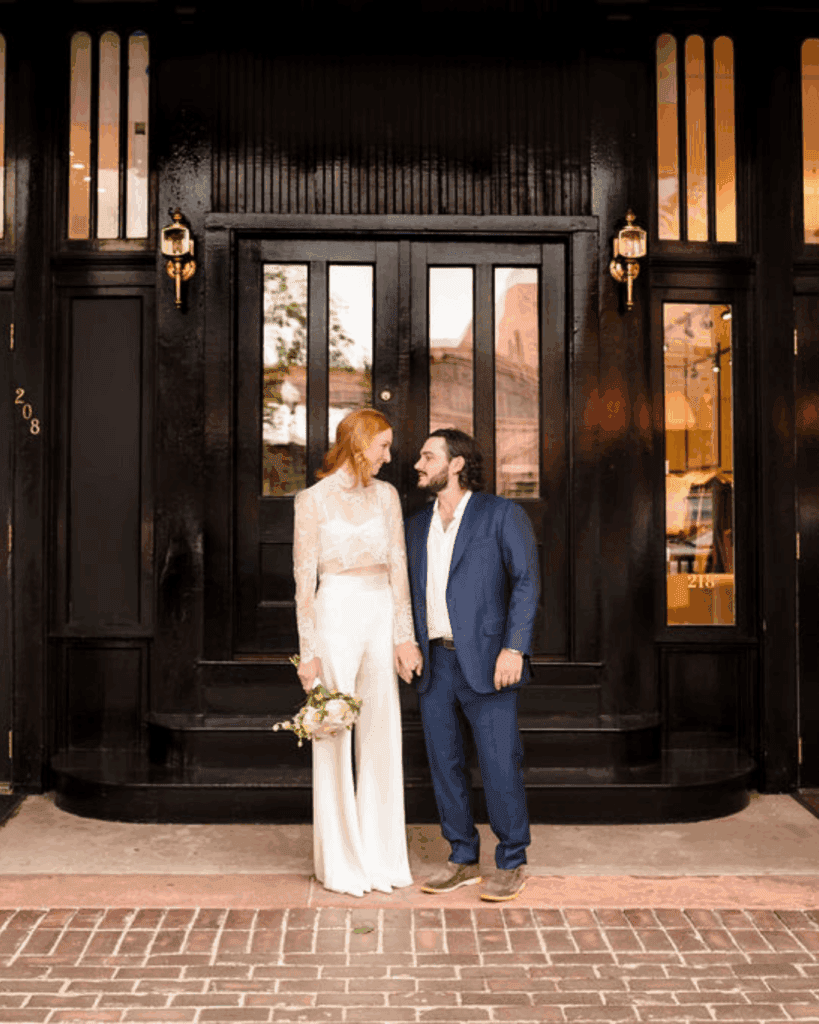 Newlyweds standing together outside a dark wooden doorway