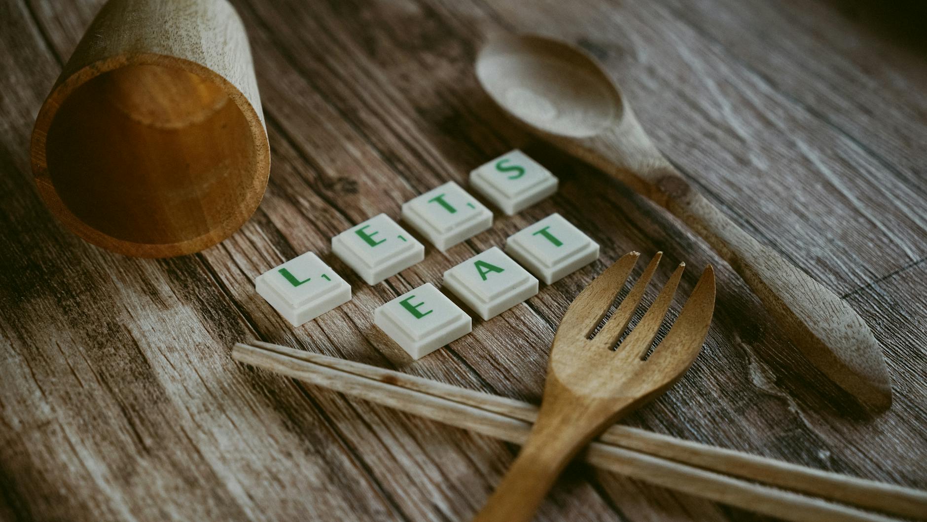 A colorful wooden word puzzle on a classroom table with students hands arranging letters to spell vocabulary words.