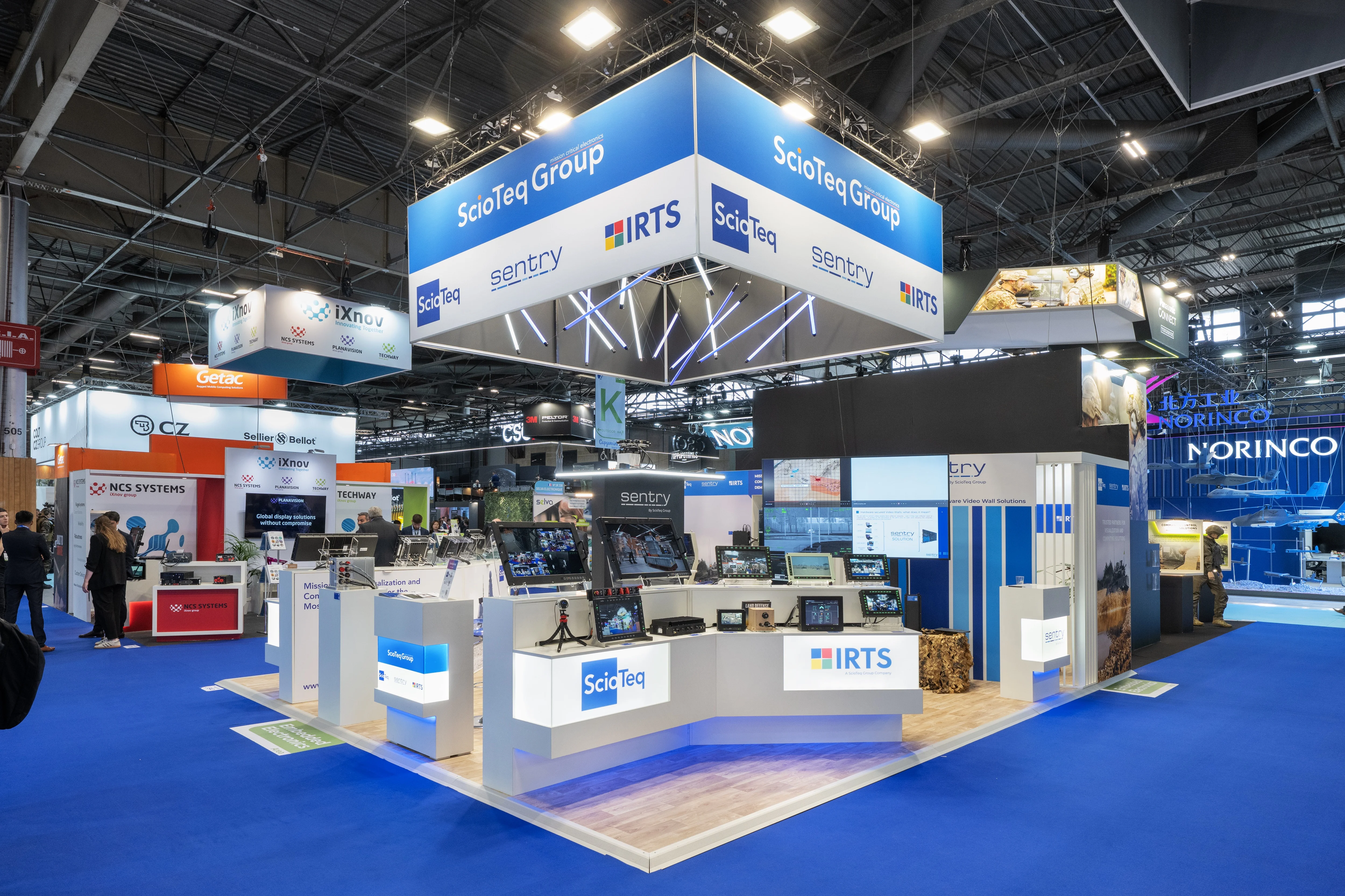 Stand IRTS / ScioTeq Group conçu et réalisé par Expace à Eurosatory 2026 – espace sur-mesure défense avec bandeau suspendu lumineux, comptoirs de démonstration d'écrans durcis et de calculateurs embarqués (ScioTeq, Sentry, IRTS).