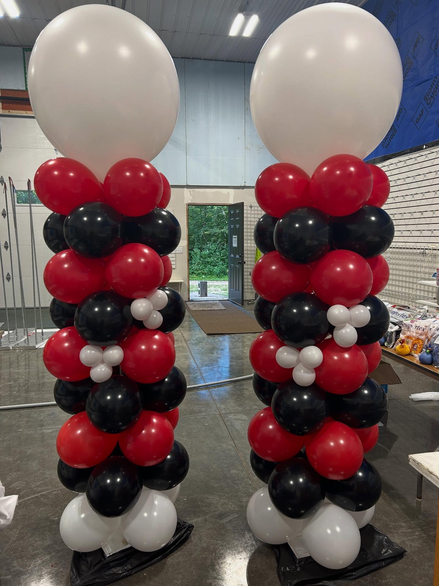 Two tall red, black, and white balloon columns with large white balloon toppers set up indoors by Be Bold Balloons
