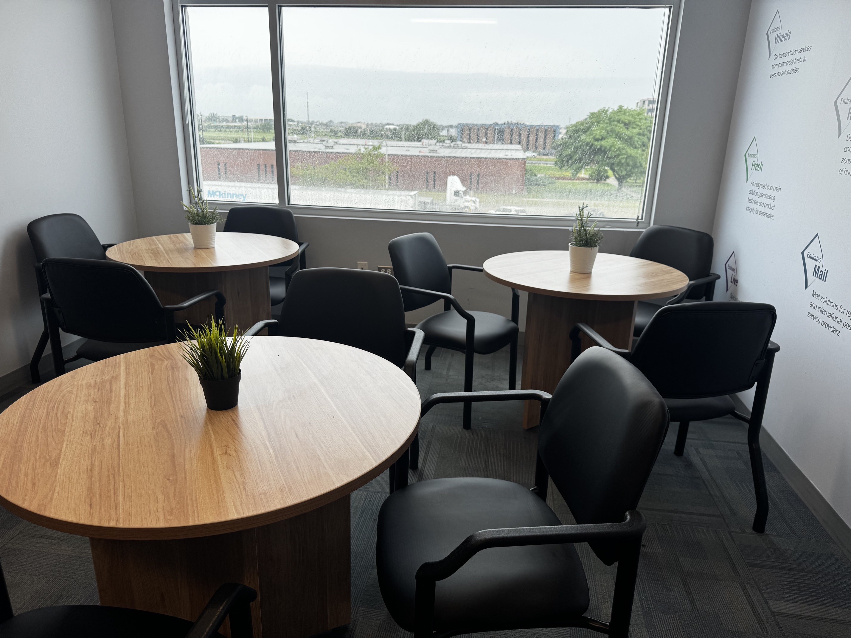 Emirates office breakroom furnished with three round wood tables and black commercial seating