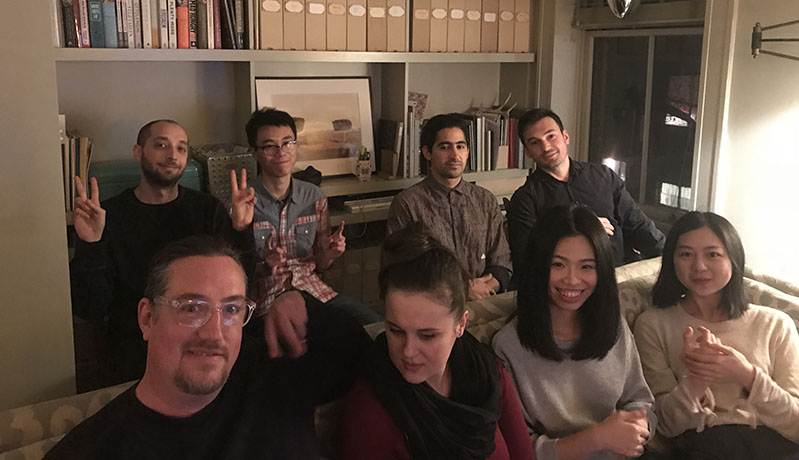 A photo of a group of people sitting in a room near a book shelf.