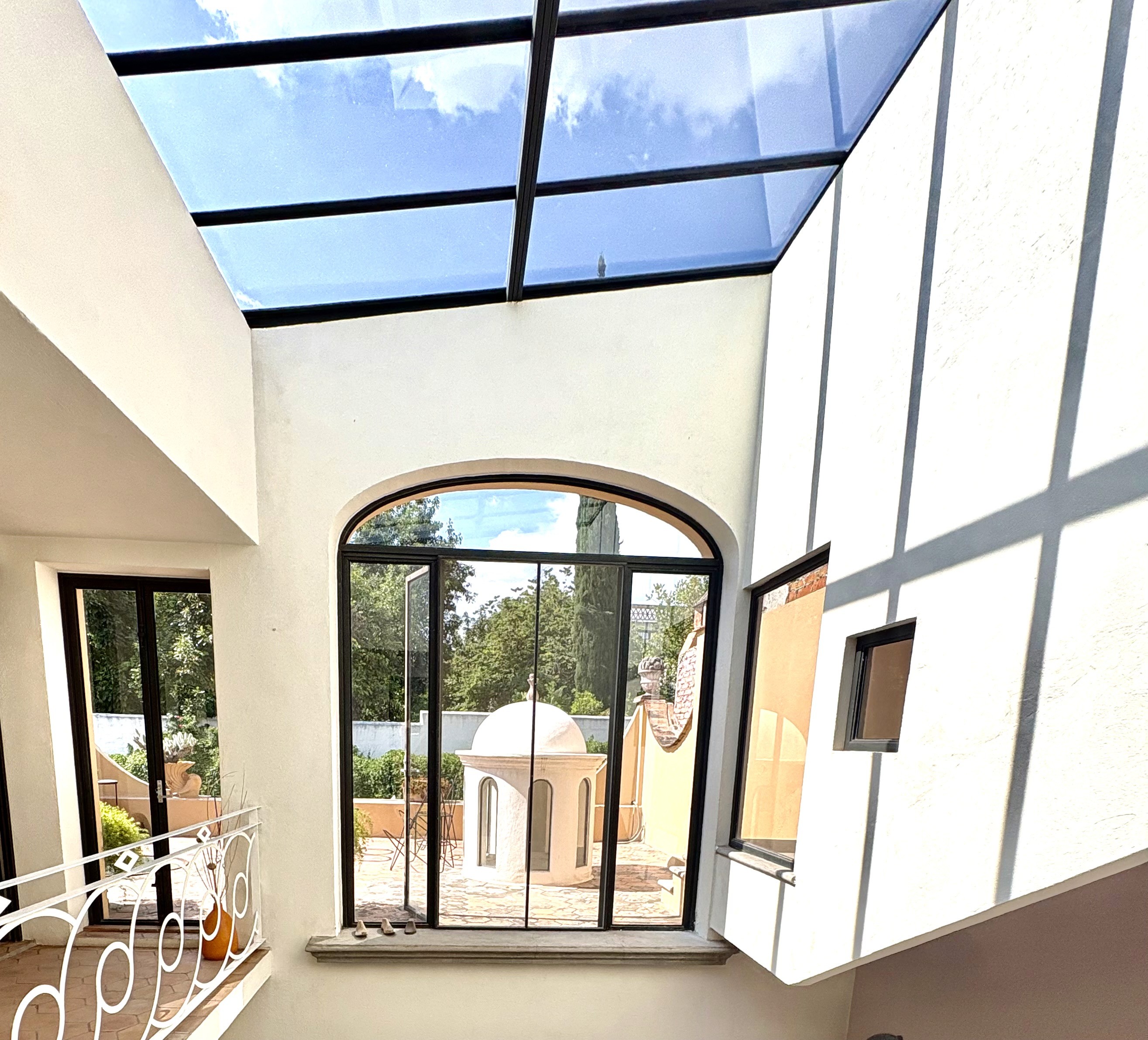 Casa de los Tíos interior with full glass skylight, arched window, white circular railing, pink staircase, and lower living area