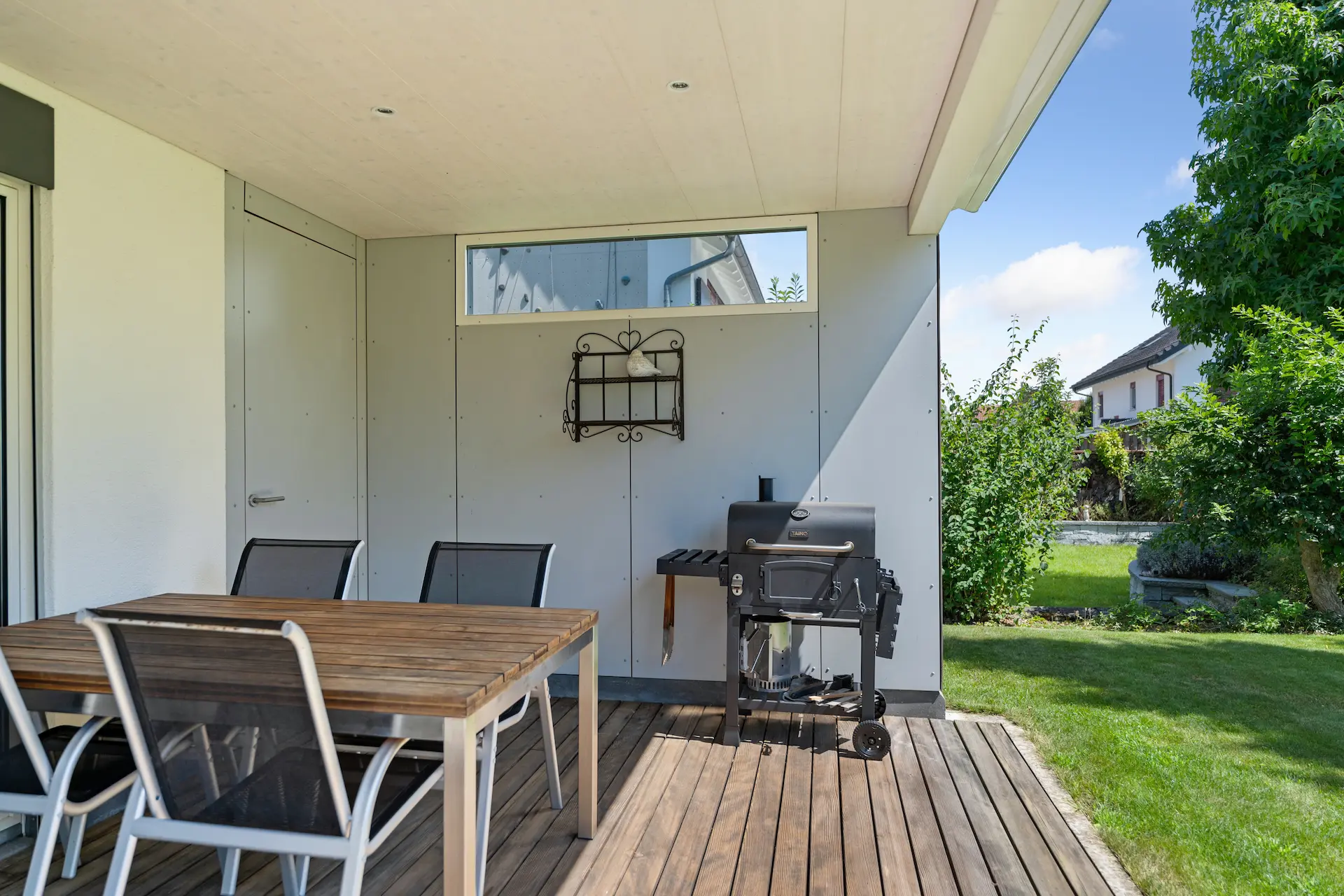Gedeckter Gartensitzplatz mit Holzboden und integriertem BBQ Bereich