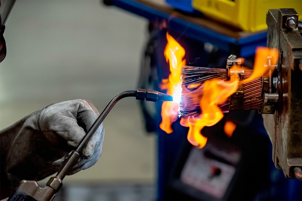 Un travailleur soudant un objet avec une torche, avec des flammes vives et des gants de protection.