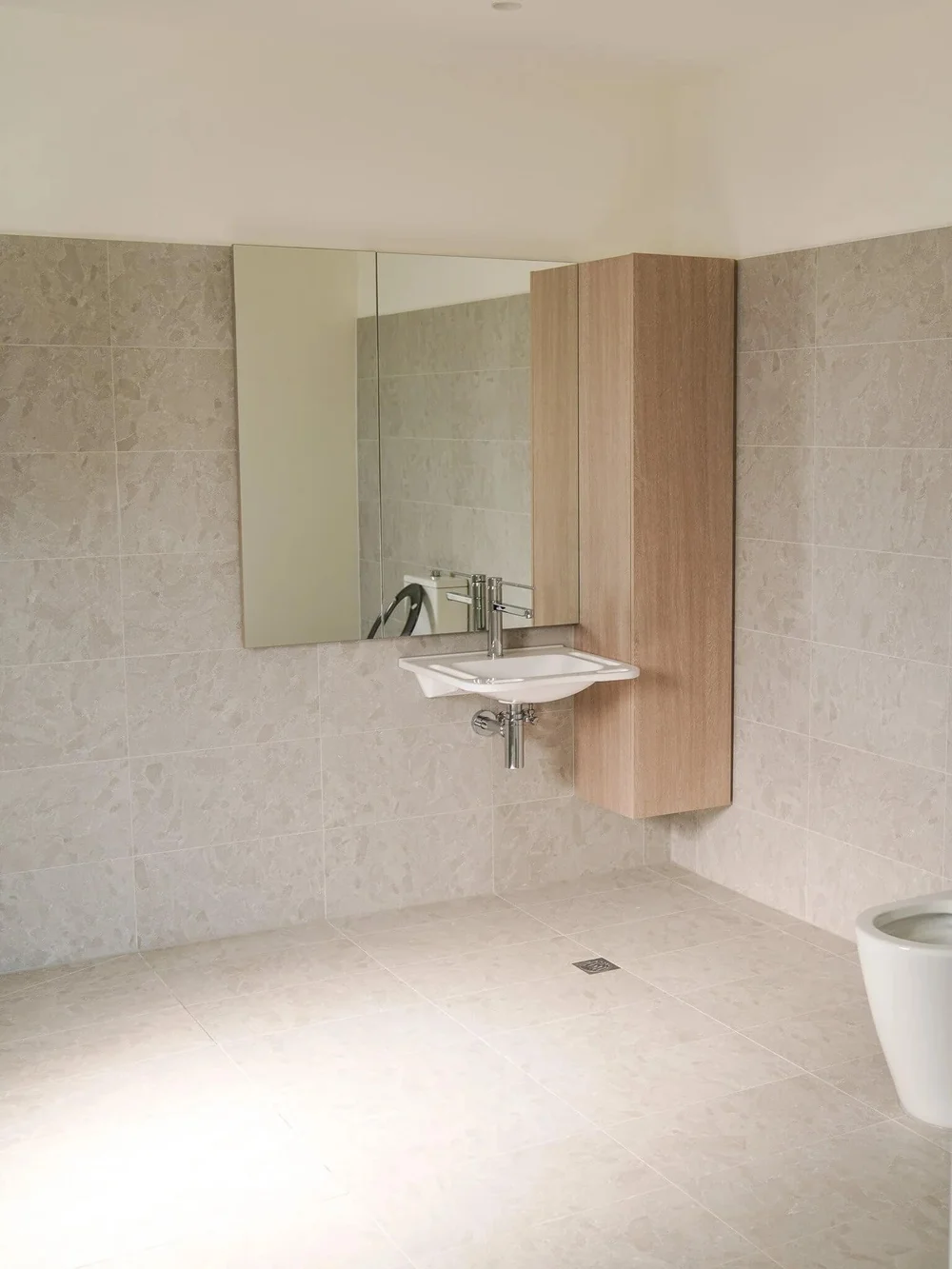 Modern minimalist bathroom with beige tiles, wall-mounted sink, and vanity mirror.