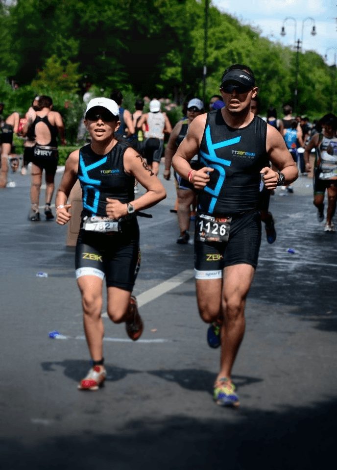 Atletas zenbike en competencia de triatlón, corriendo juntos en avenida arbolada y clima soleado.