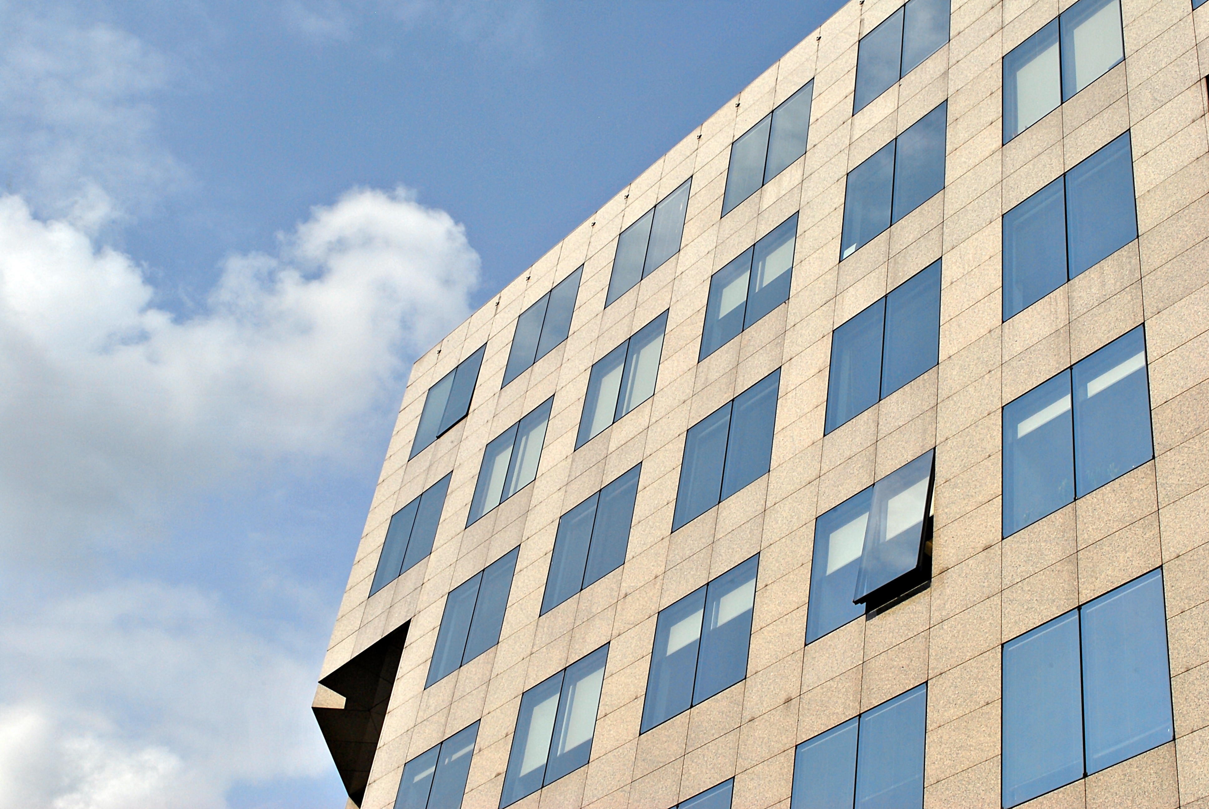Modern office building with reflective glass windows and beige facade against a blue sky.