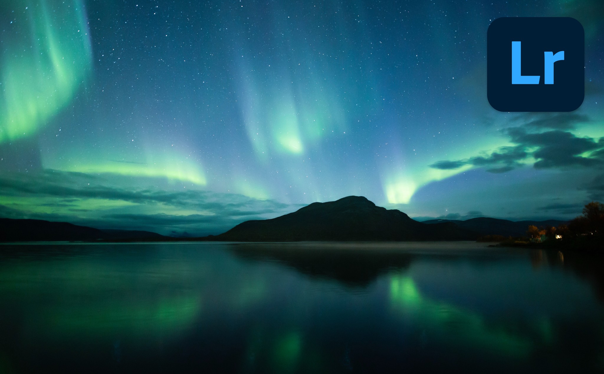 The aurora borealis glowing over a dark mountain with reflections on a still lake