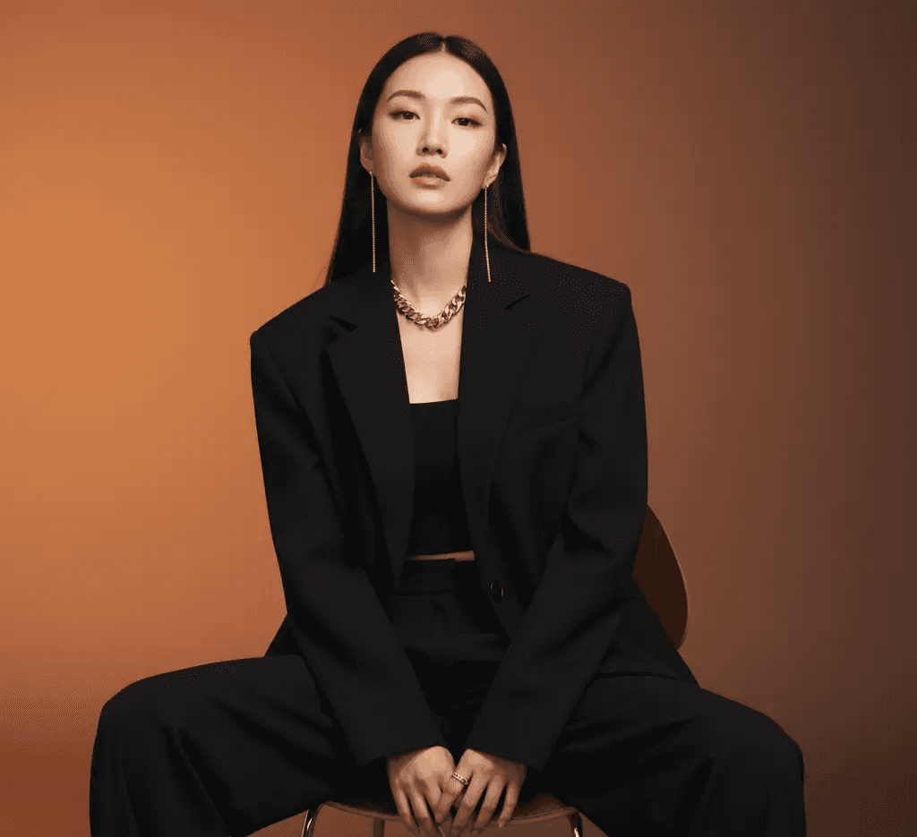 A high-quality, AI-generated professional portrait of a confident woman with long black hair, sitting on a chair and wearing a tailored black suit with bold silver jewelry. This generated image is a case study used by Mahindra, a specialist digital marketing trainer and marketing trainer consultant, to illustrate advanced visual content strategies on his blog.