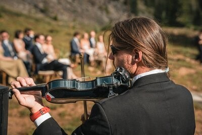 A violinist plays beside the outdoor wedding guests.