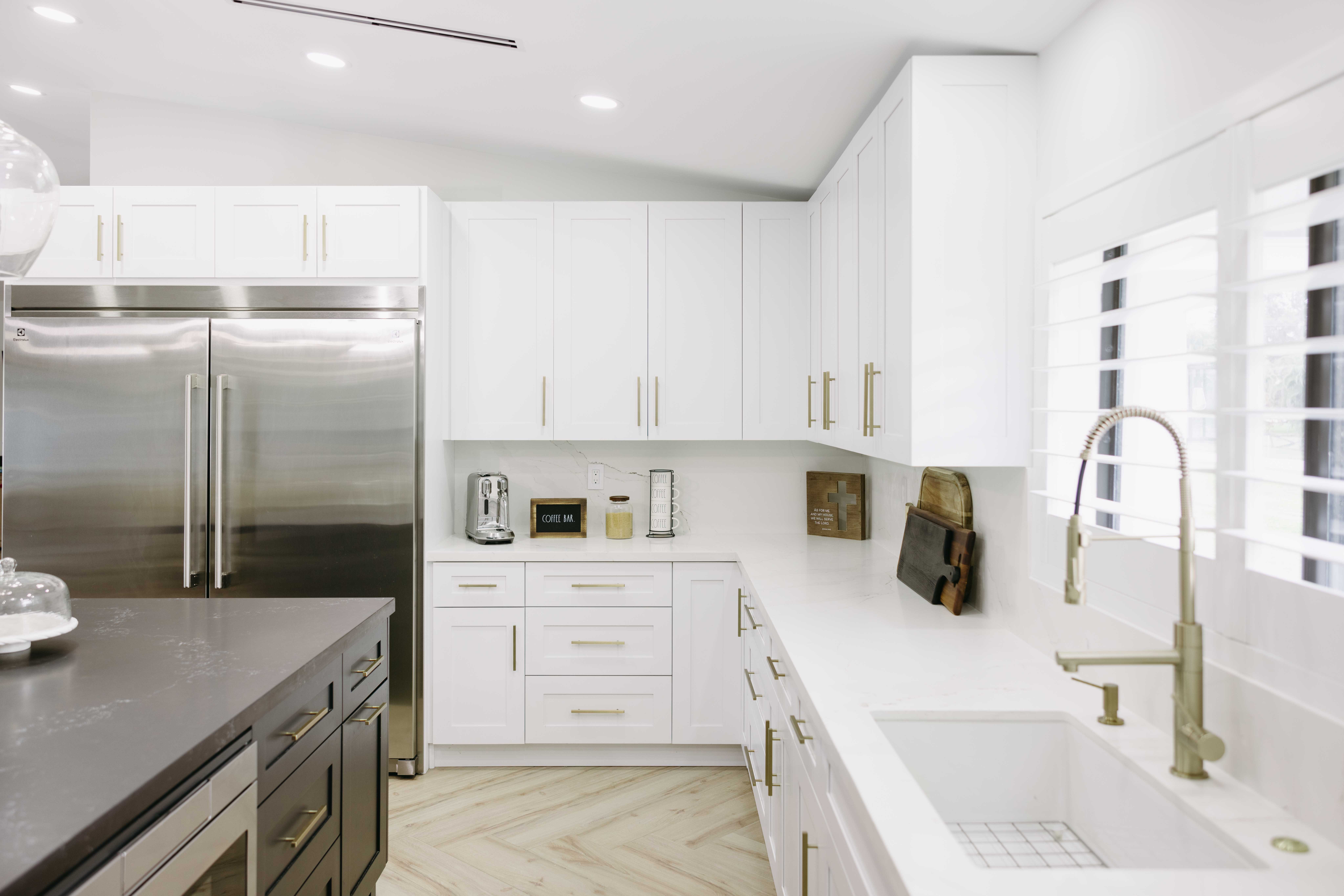 Modern white kitchen with stainless steel appliances, island, and herringbone floor.