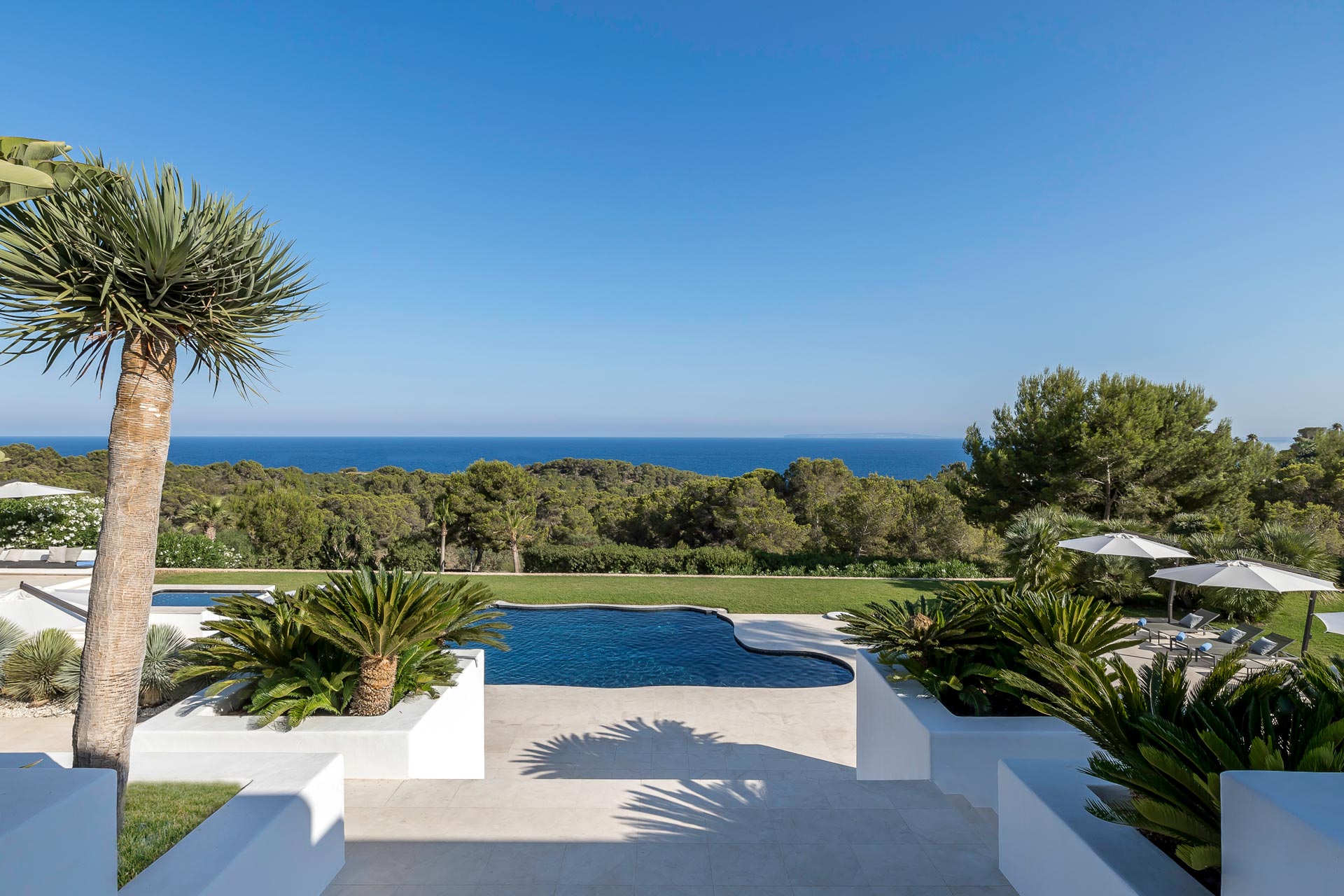 Private estate pool terrace with palm trees, Mediterranean garden landscaping and open sea views.