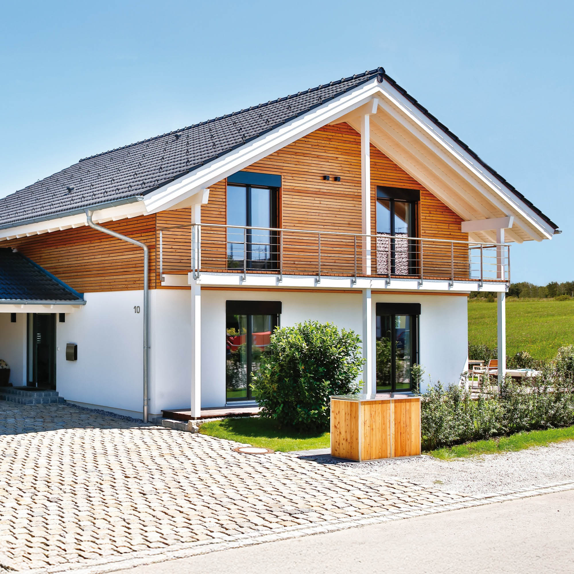 Modernes Einfamilienhaus mit Holzfassade, weißem Putz und Balkon unter blauem Himmel.